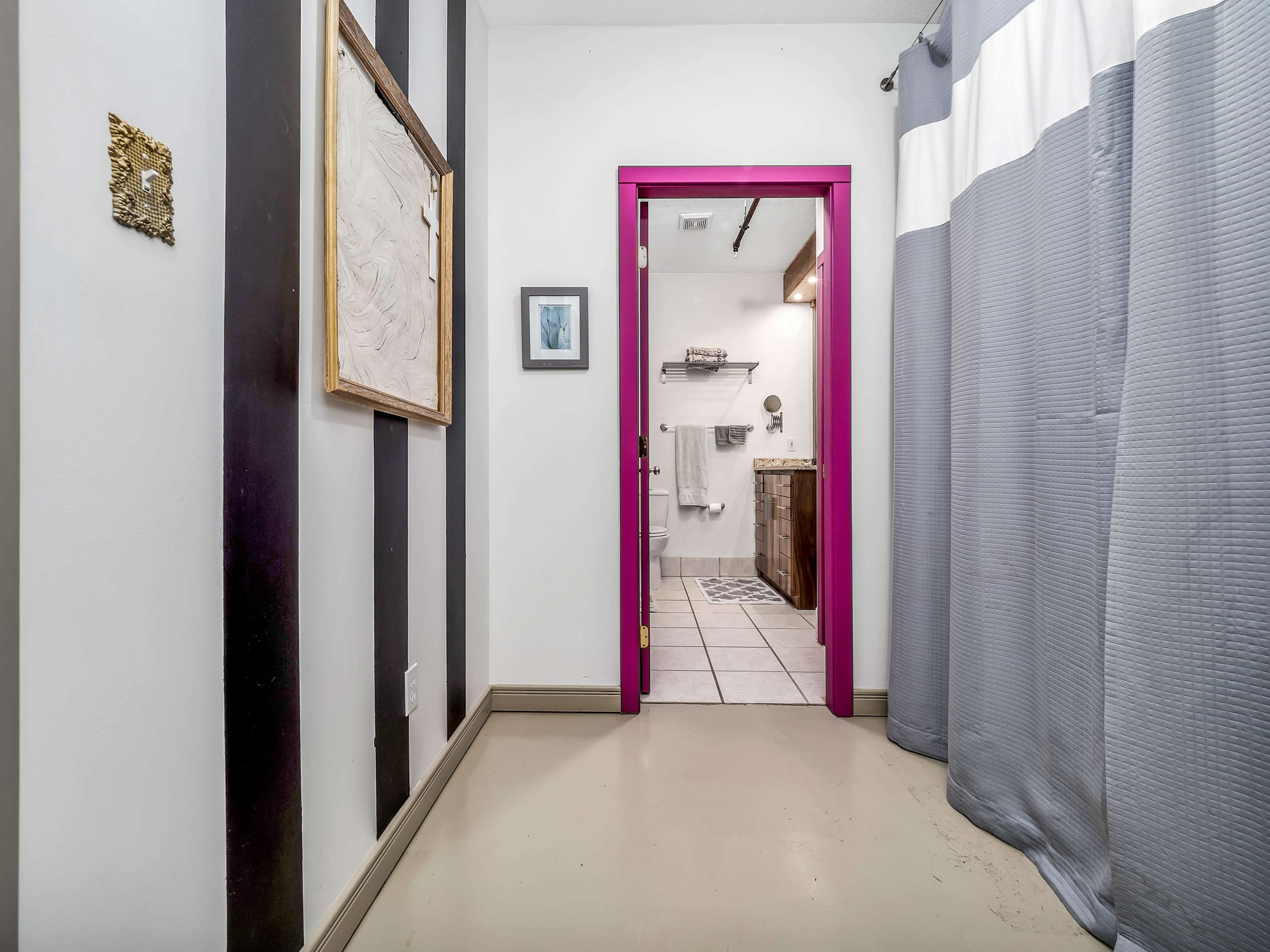 A hallway leads to a brightly framed doorway opening into a bathroom, with a gray and white patterned curtain partially covering the entrance.