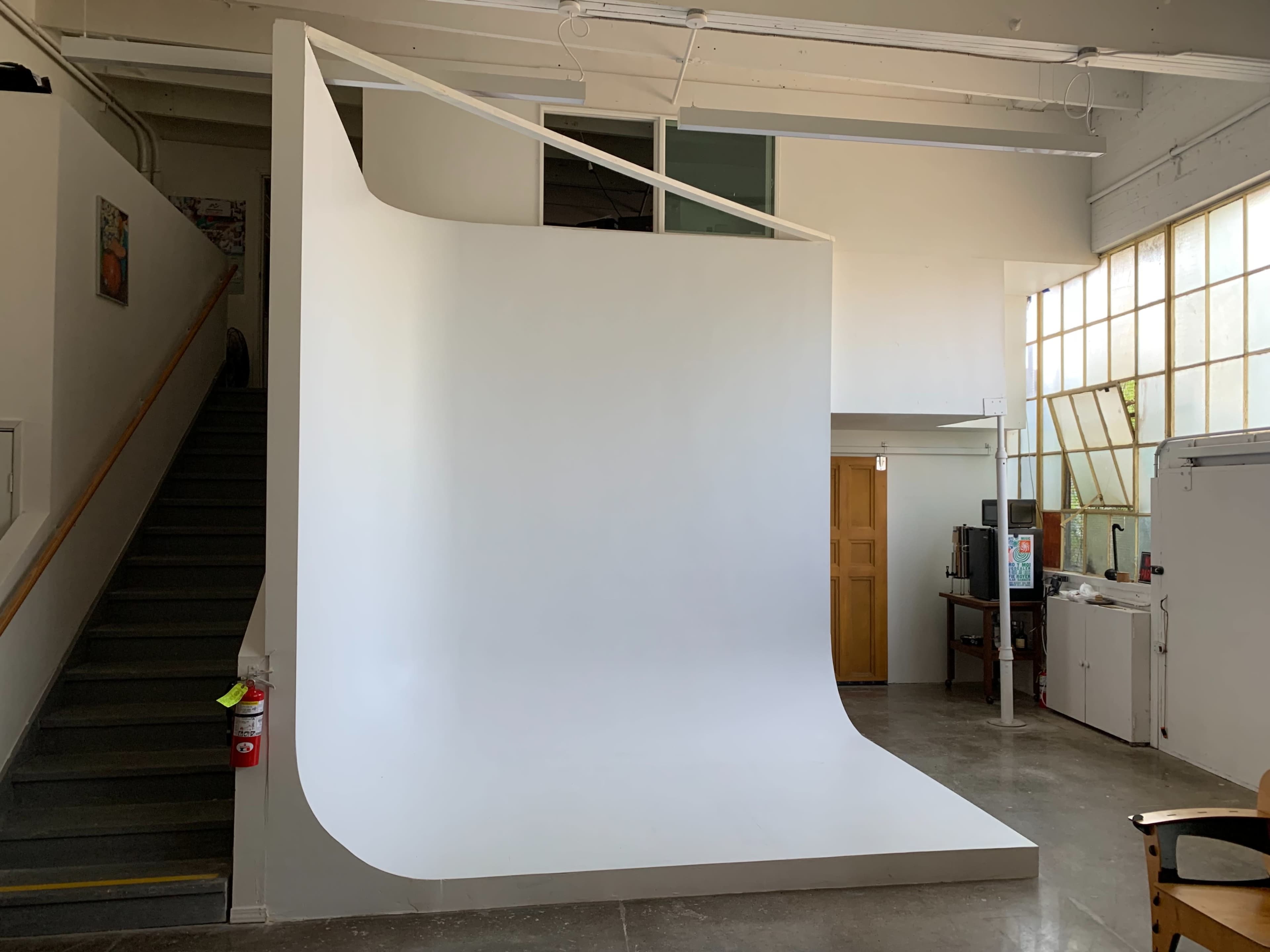 The image shows a large white curved backdrop within a spacious, well-lit studio setting.