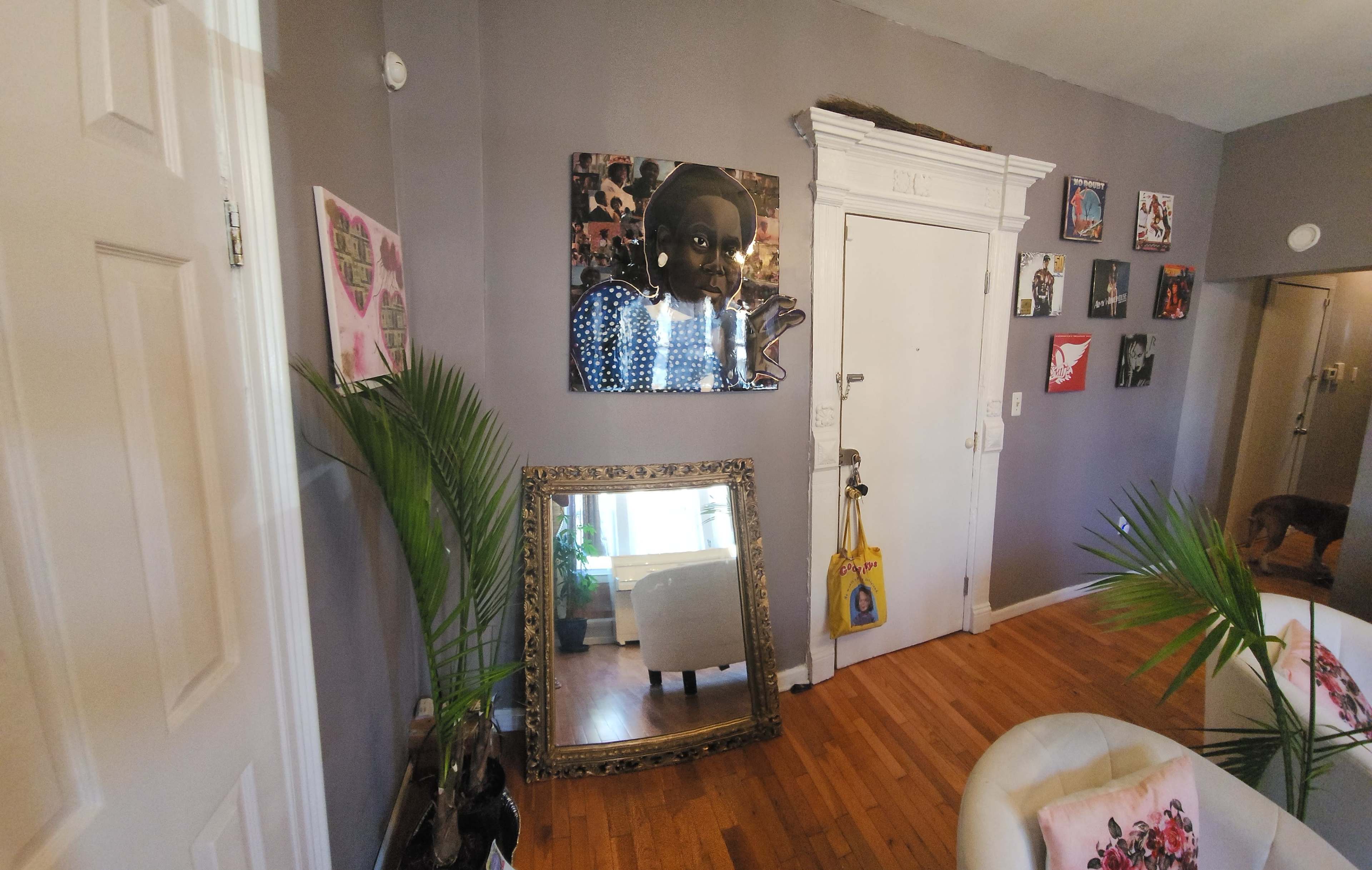 A living room with gray walls, featuring a large mirror and several framed artworks, along with plants and furniture.