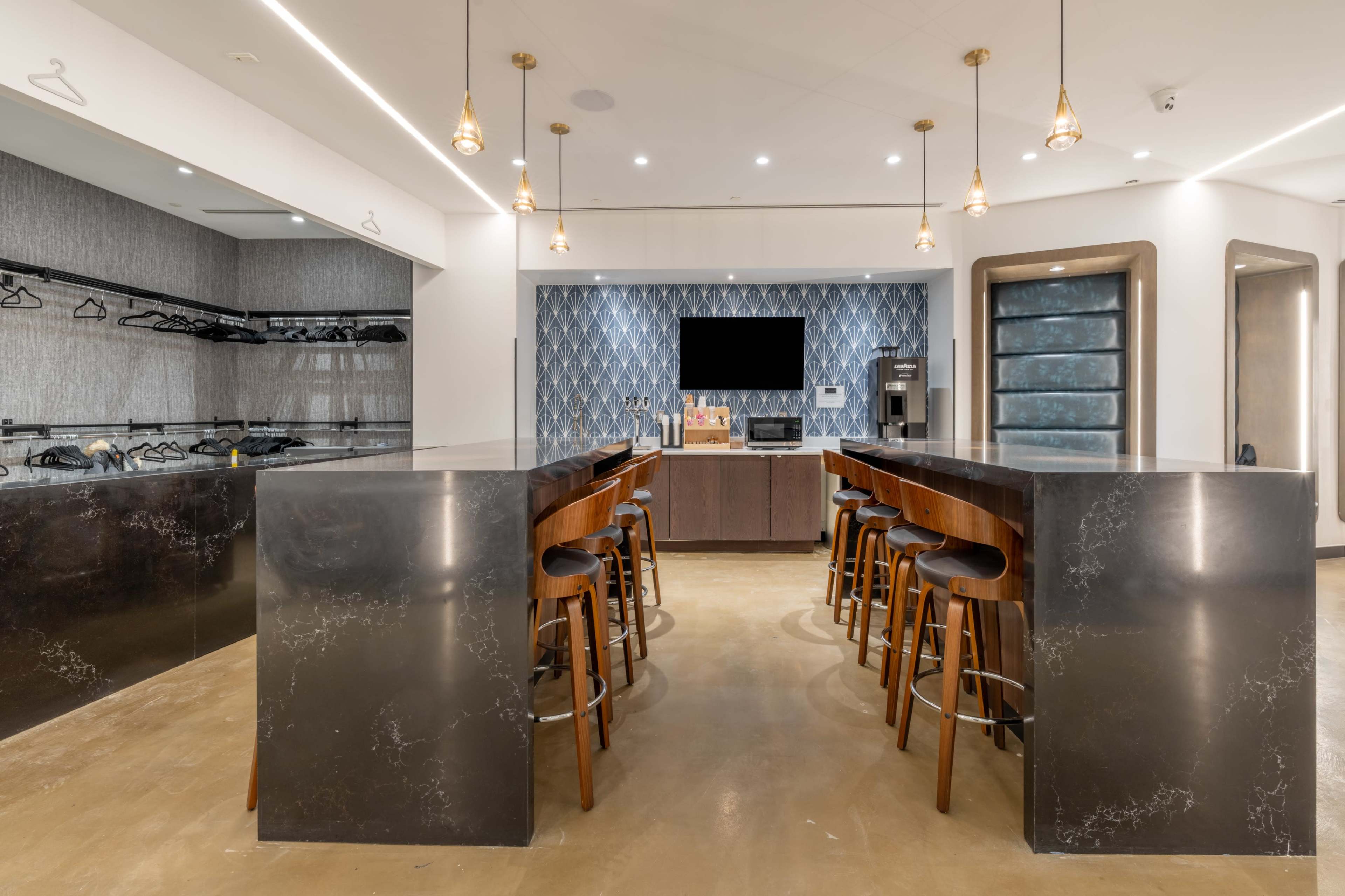 The image shows a modern kitchen area with a large island bar featuring several wooden stools and a wall-mounted television.
