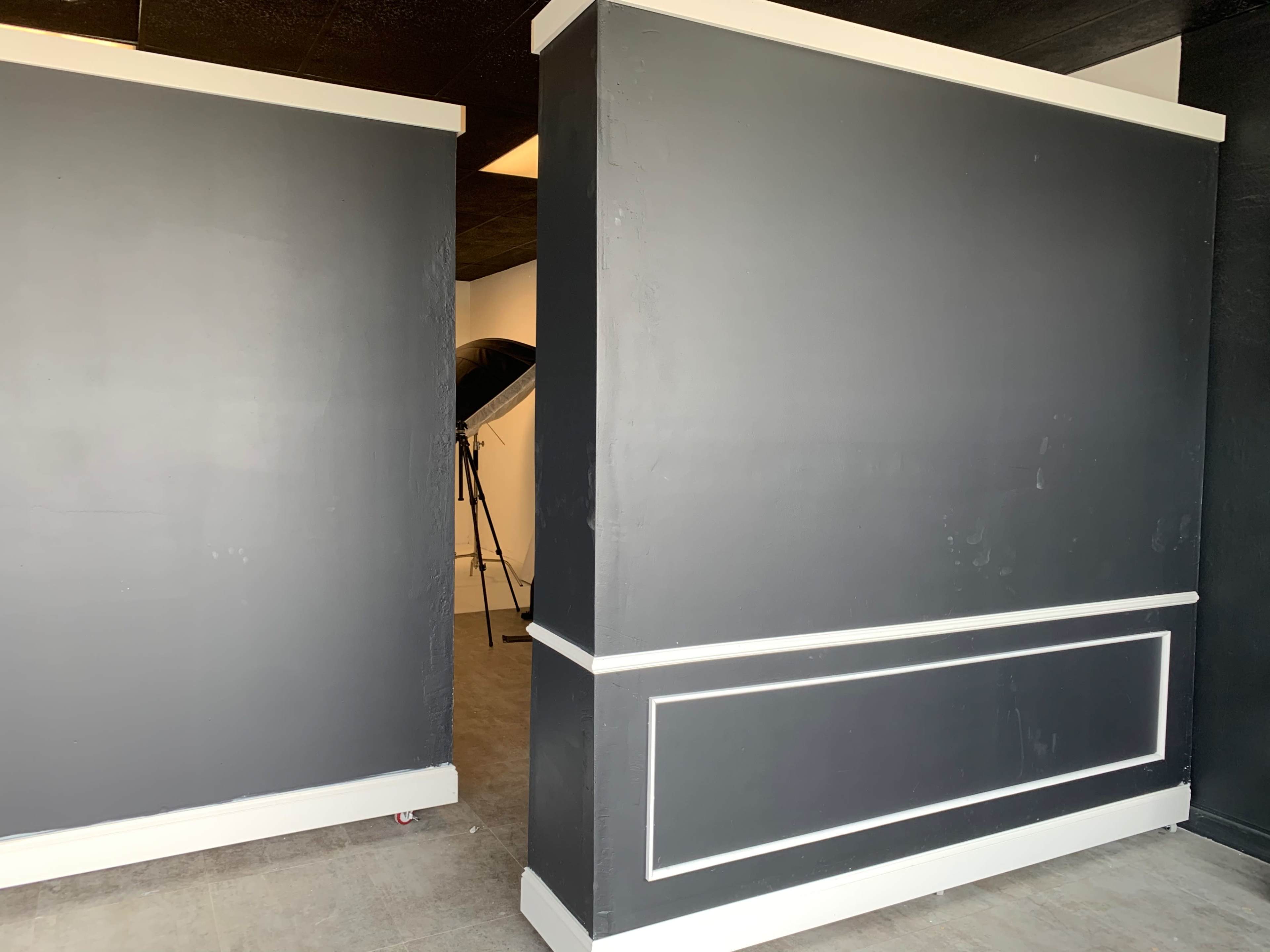 Two large black walls with white trim in a sparsely furnished studio space.