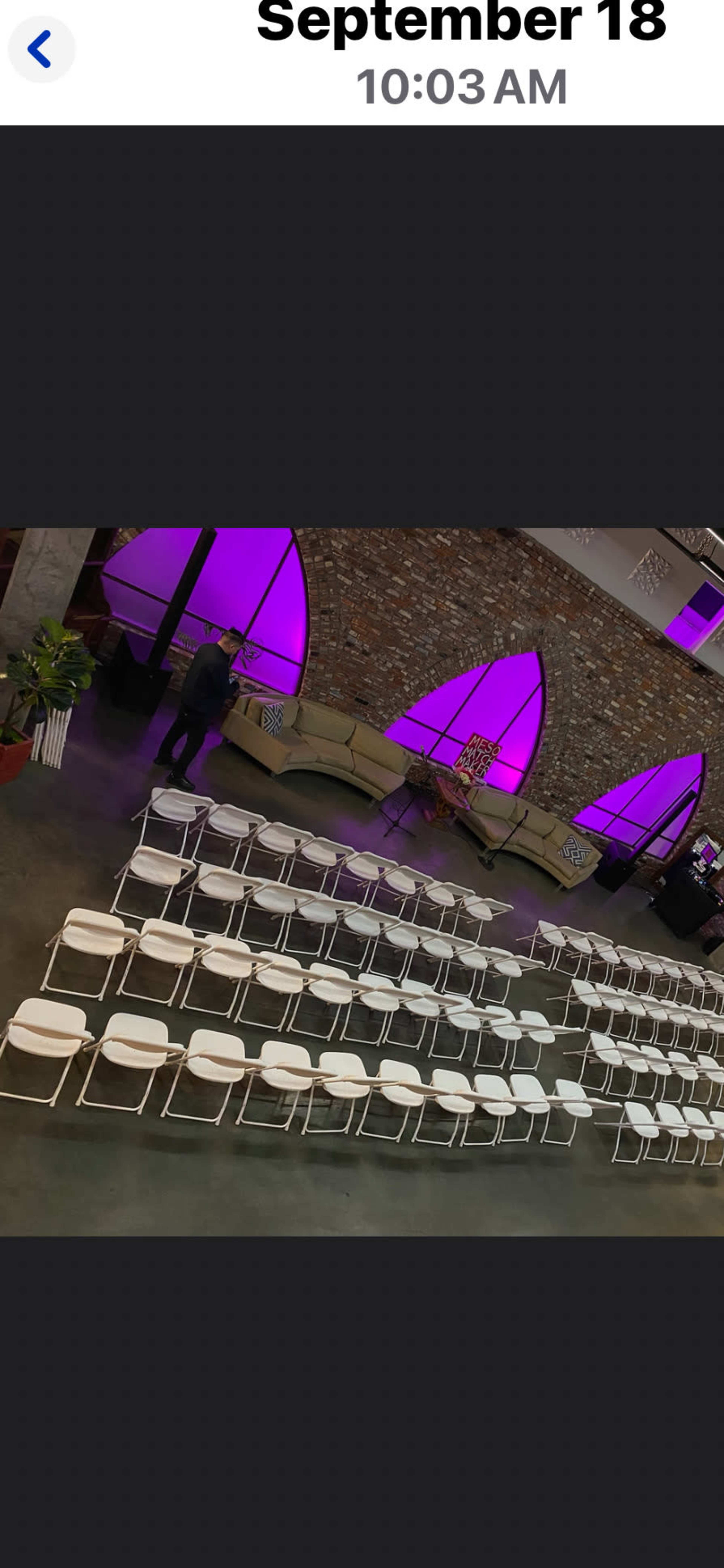 The image shows a spacious venue with rows of white chairs arranged for an event, accompanied by a stone wall and purple-lit decorative features.