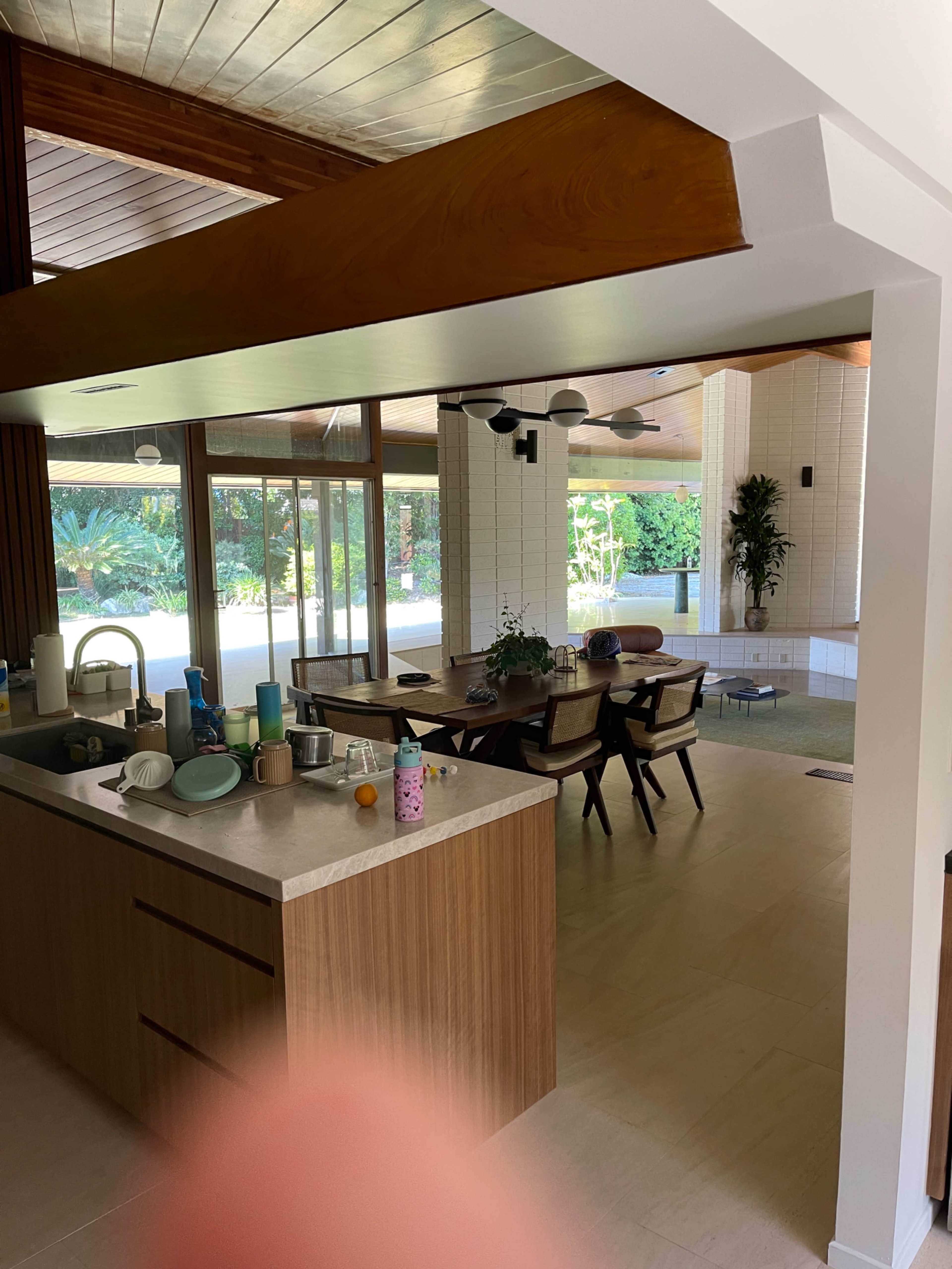 A modern kitchen opens into a dining area with a large table and views of a green outdoor space.