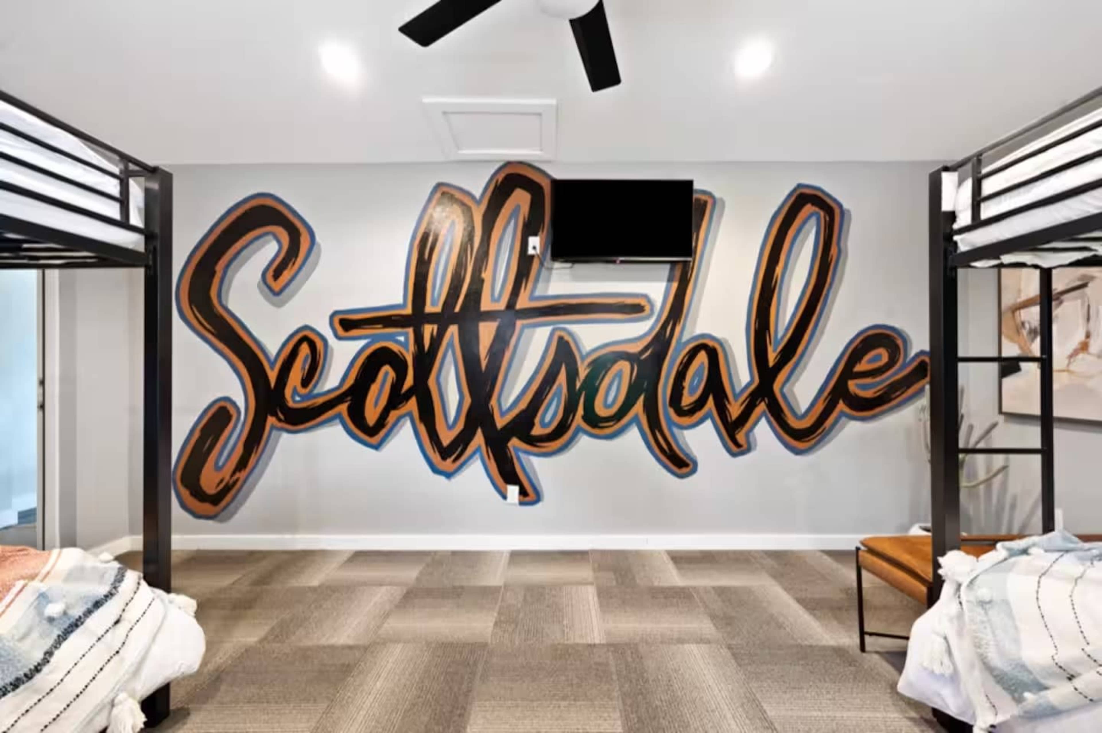 The image features a wall mural with the word "Scottsdale" written in large, colorful lettering, alongside two bunk beds and a ceiling fan in a modern room.