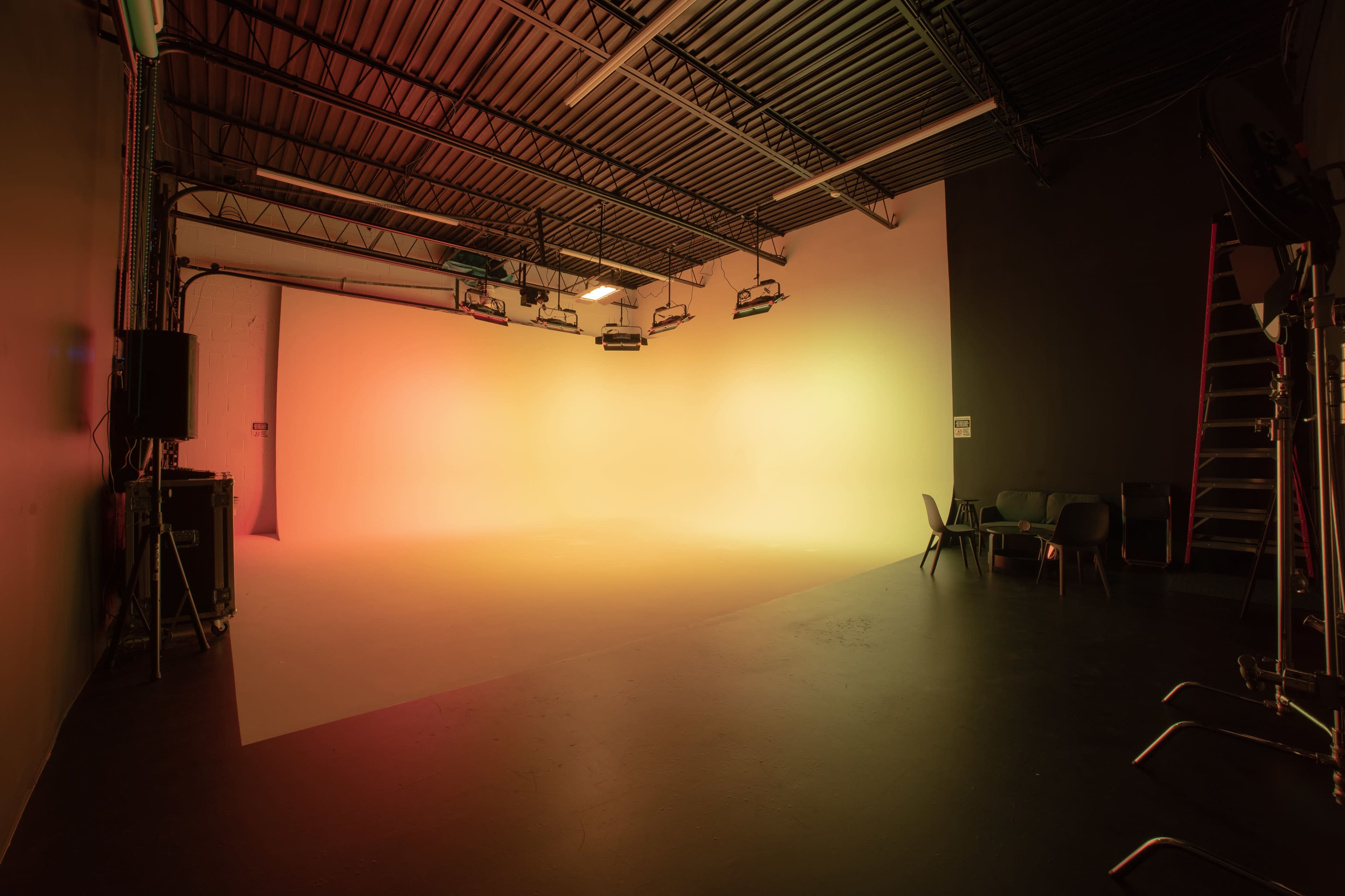 A spacious photography studio with a gradient-lit backdrop and minimal furniture in one corner.