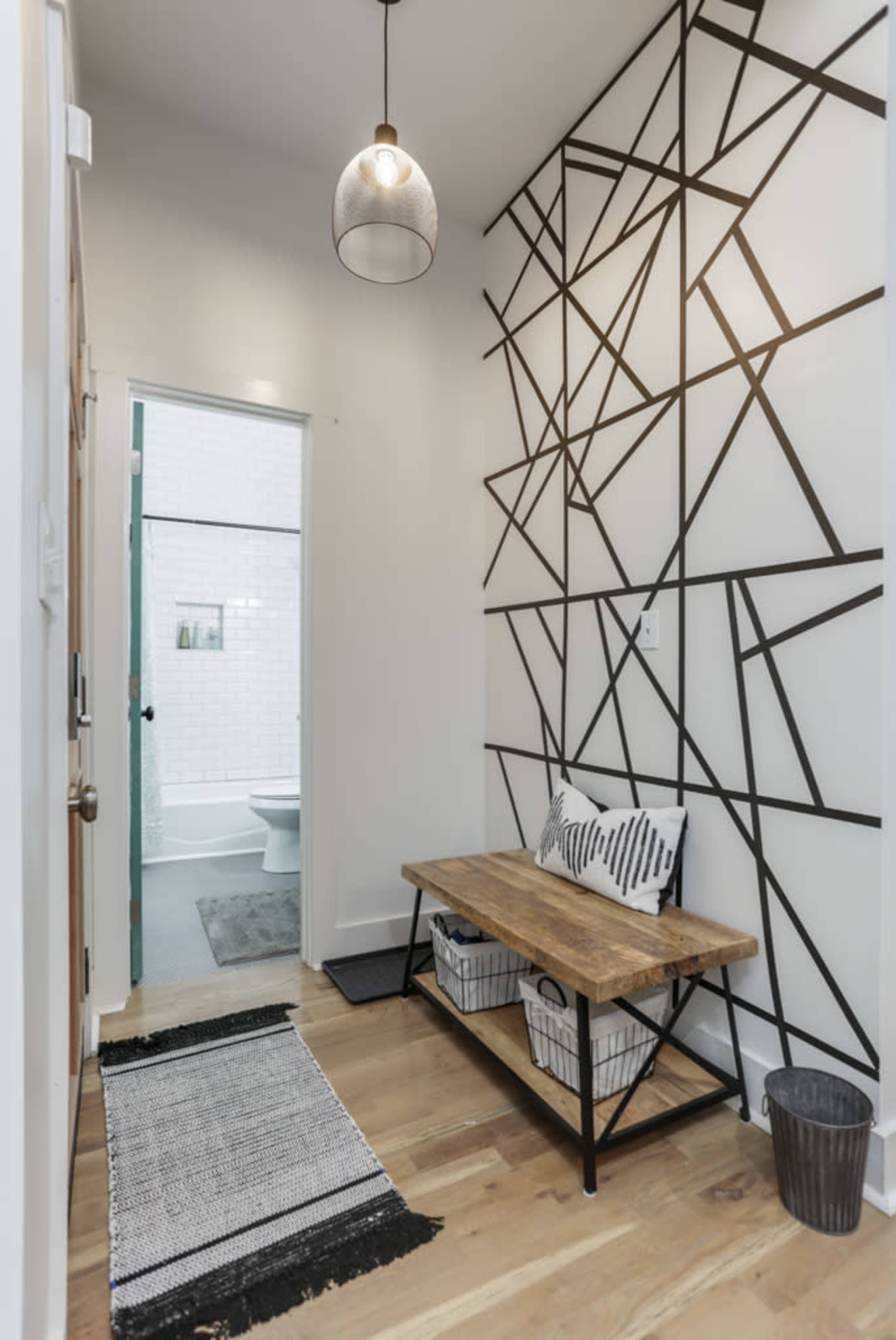 A hallway features a geometric black-and-white accent wall, a wooden bench, and a view into a bathroom.