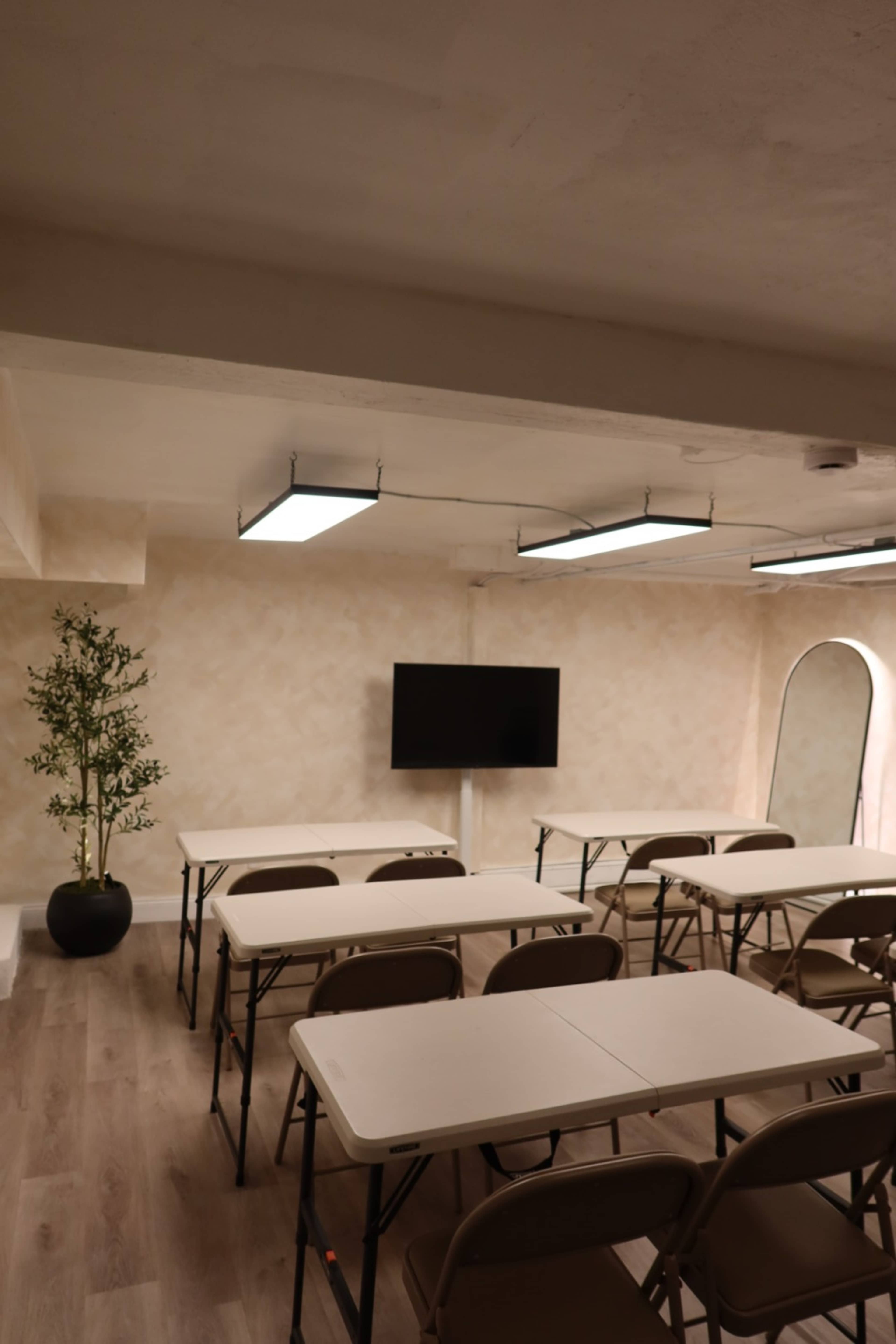 The image shows a seminar room with several folding tables and chairs arranged facing a wall-mounted television.