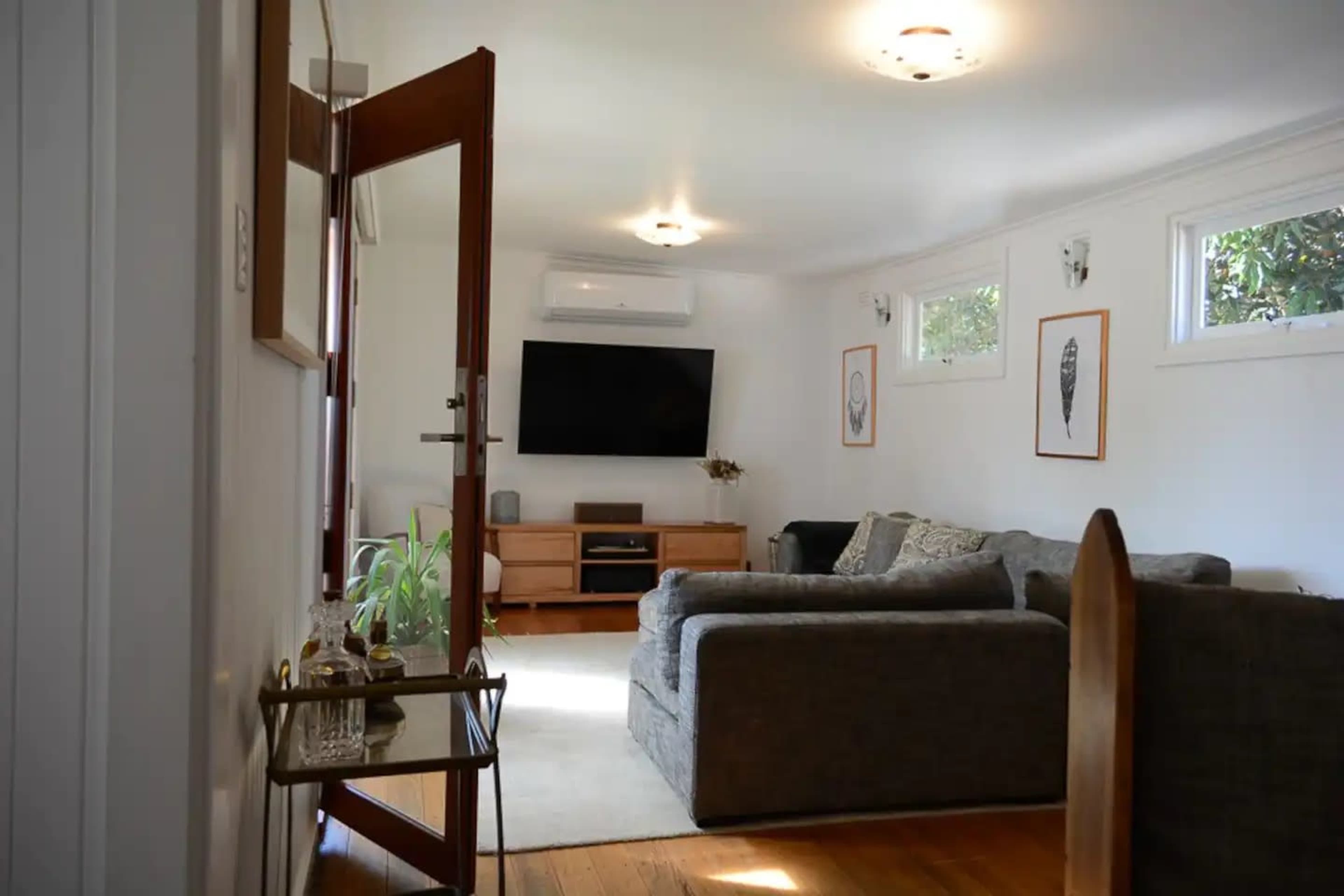 The image shows a living room with a sofa, a television mounted on the wall, and a doorway leading outside.