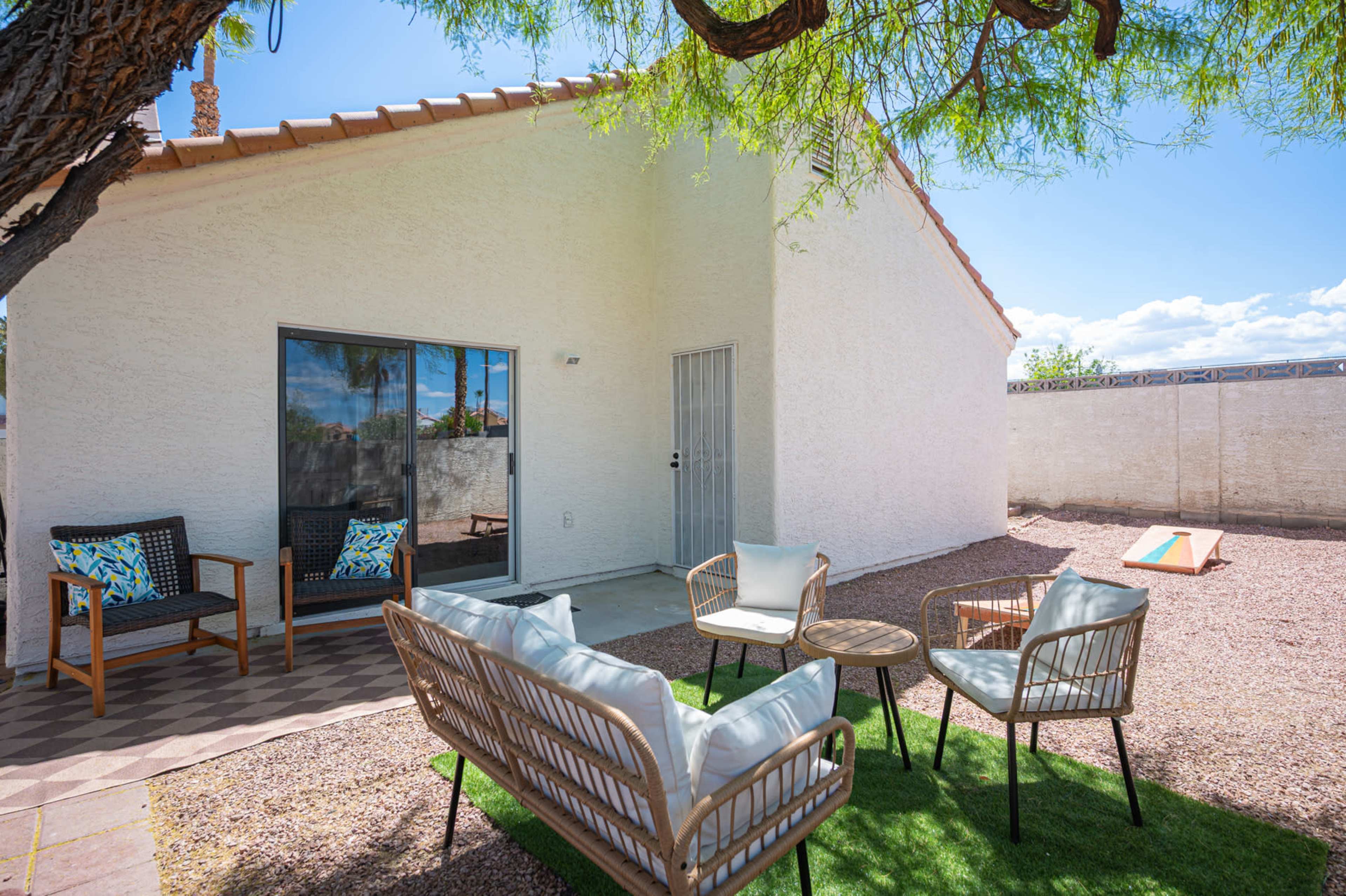 A cozy outdoor seating area with rattan furniture and a small table, set on a gravel surface next to a white house.