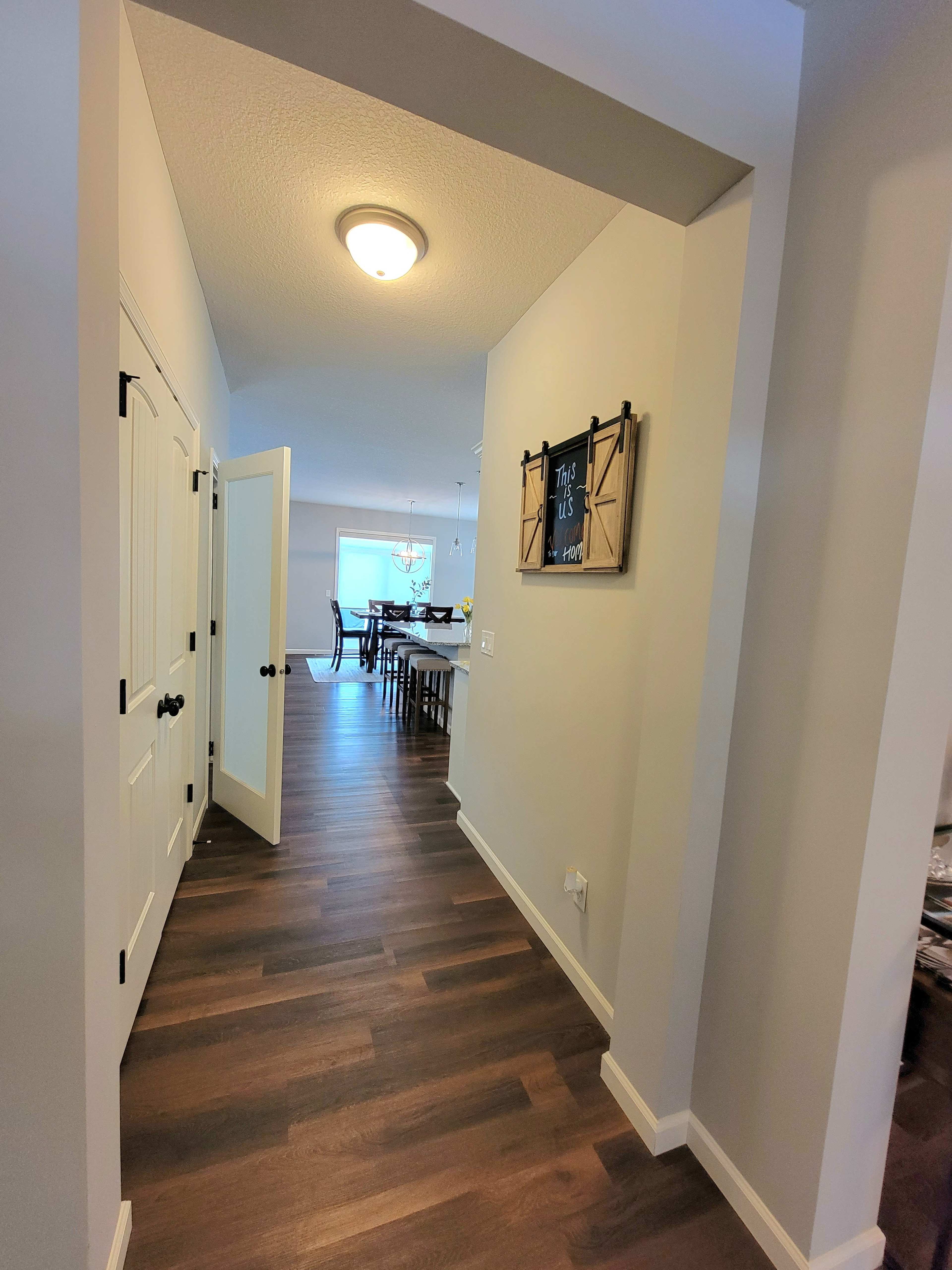 A hallway with a light fixture and a blackboard on the wall leads to a dining area at the end.