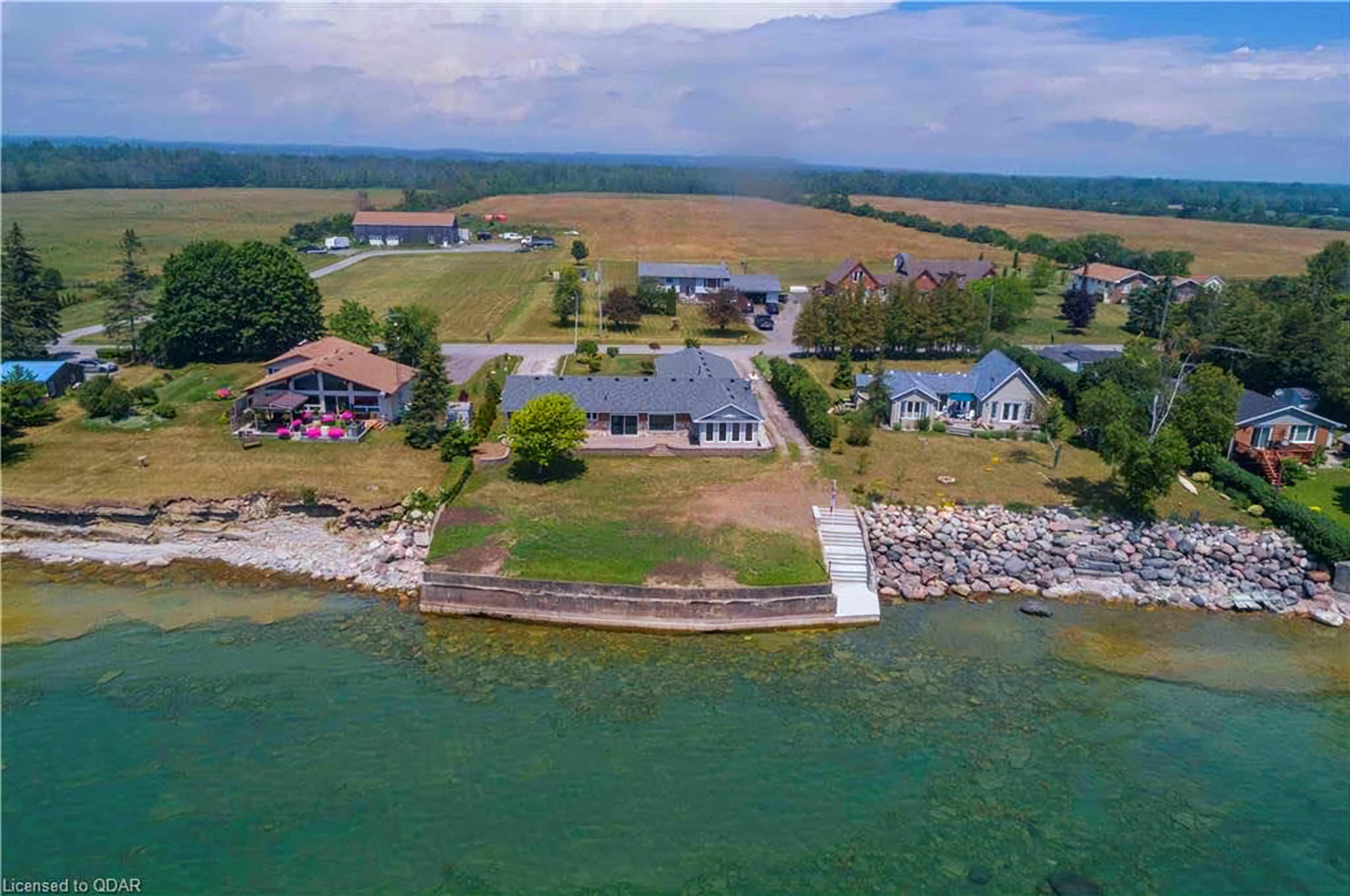 A waterfront property with a house and a landscaped yard, surrounded by fields and several nearby buildings.