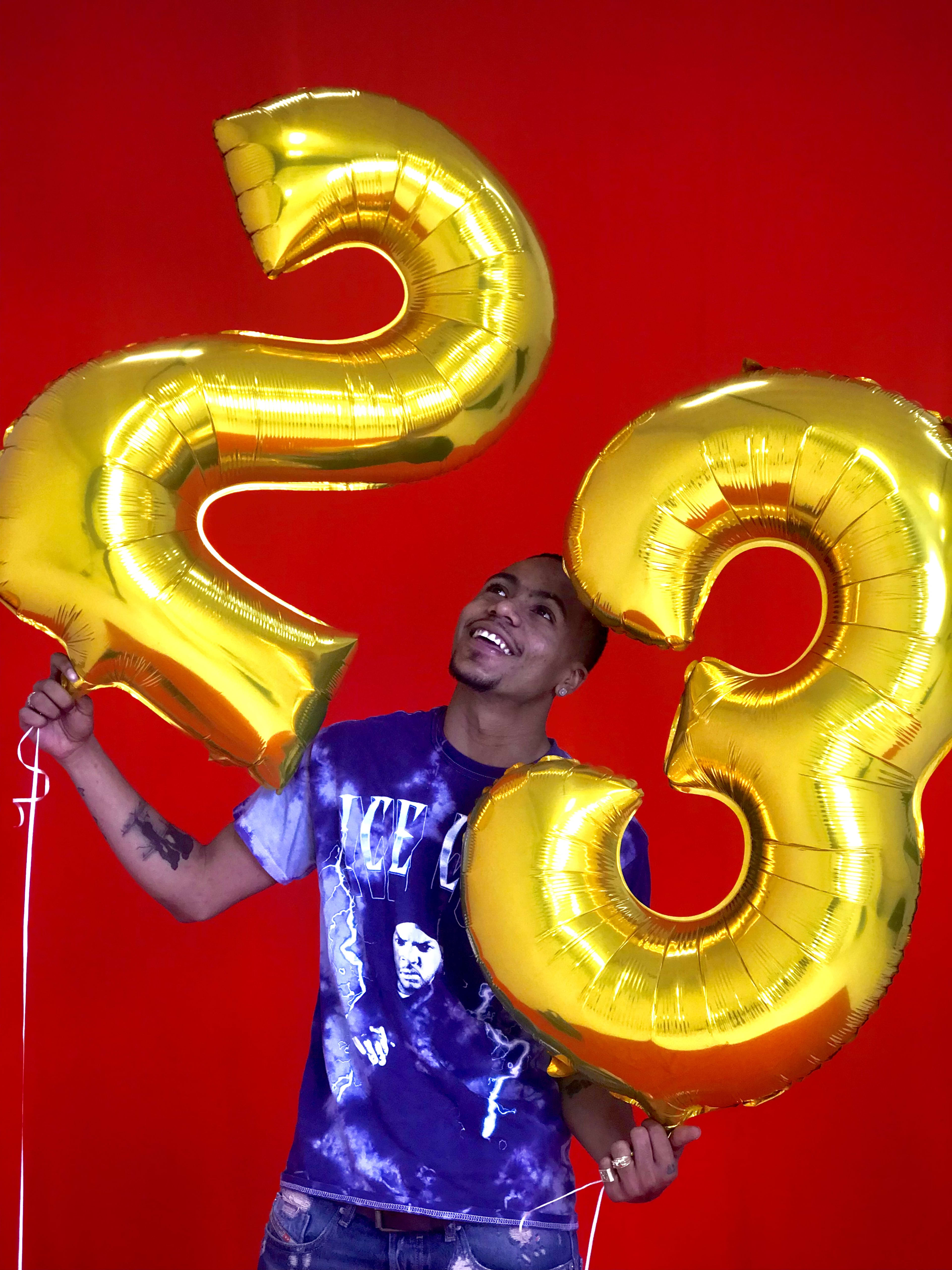 A man holding a bunch of balloons in front of a red background for a birthday photoshoot.