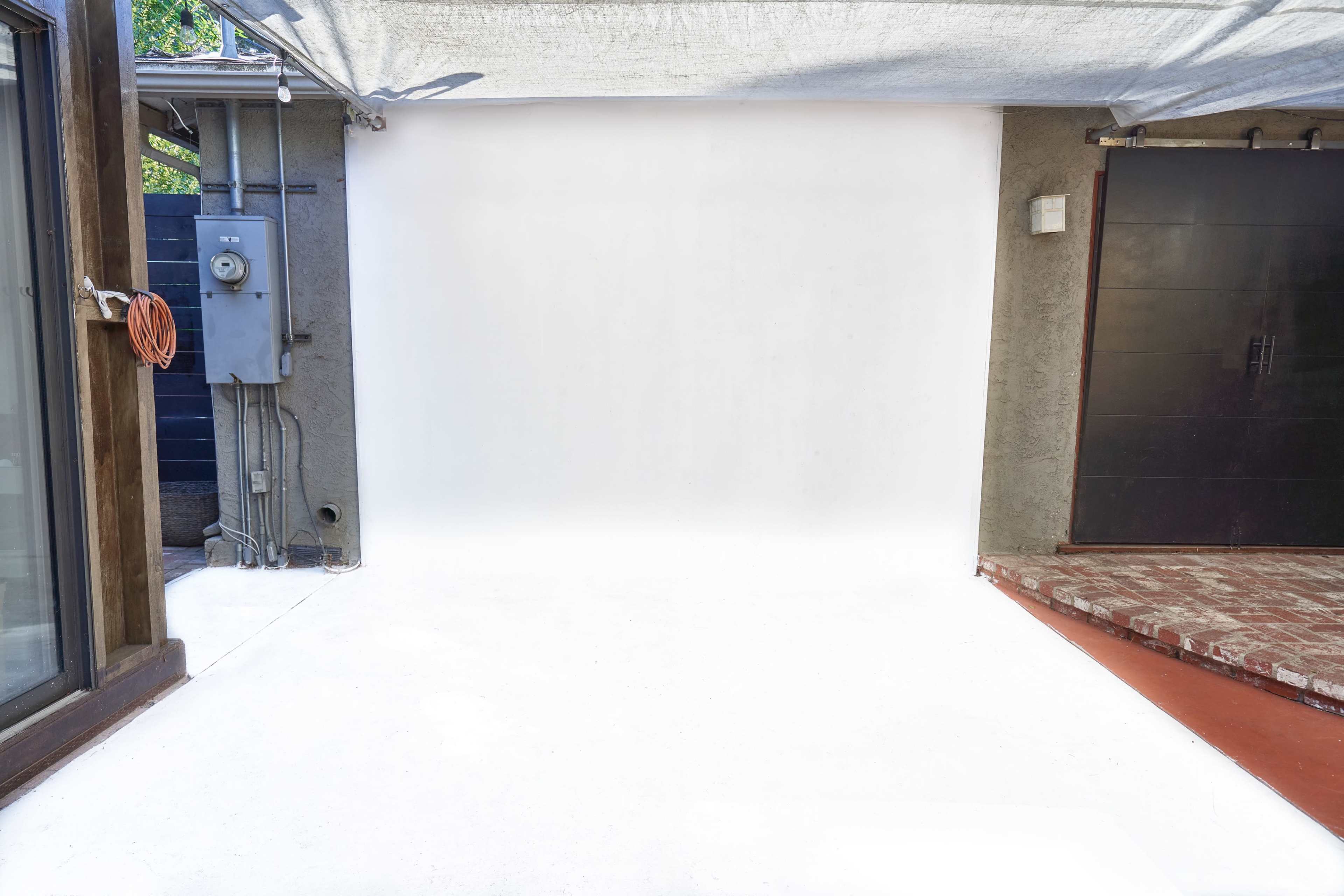 A white backdrop set up in an outdoor space, with one side featuring a door and a power meter on the wall.