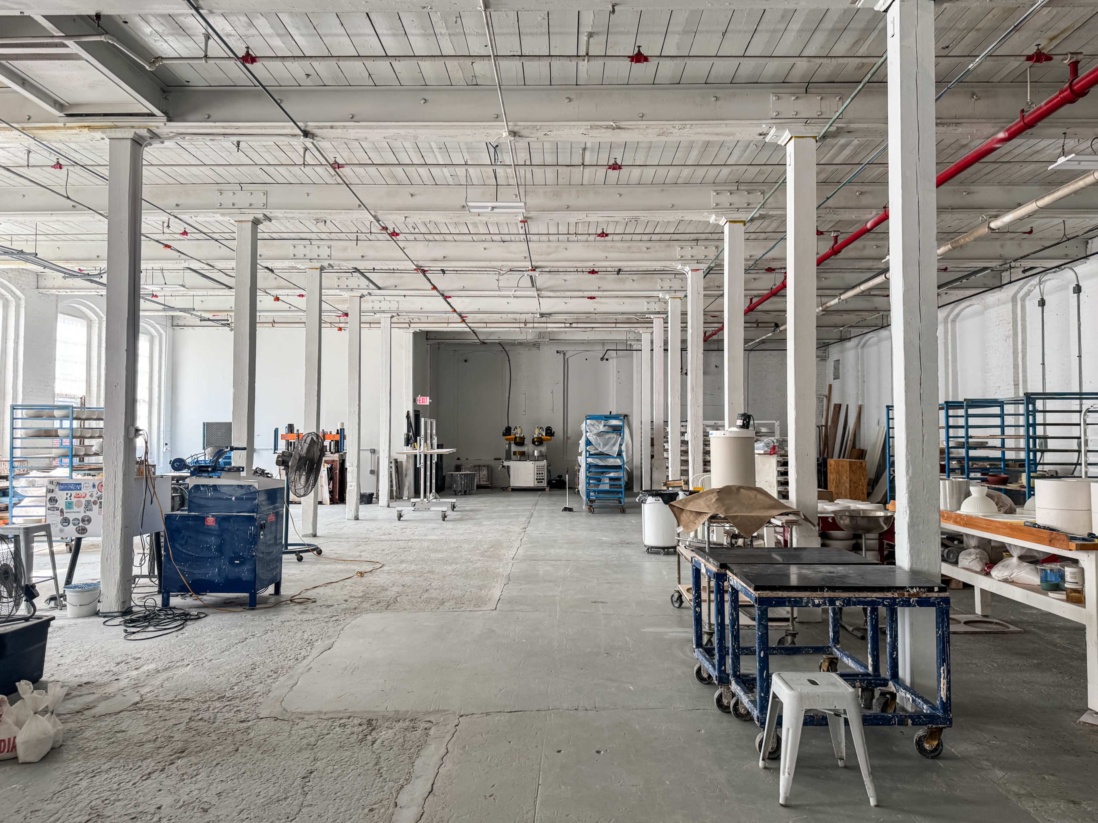 The image shows a spacious industrial workshop with tall ceilings, empty workstations, and various tools and equipment arranged throughout the room.