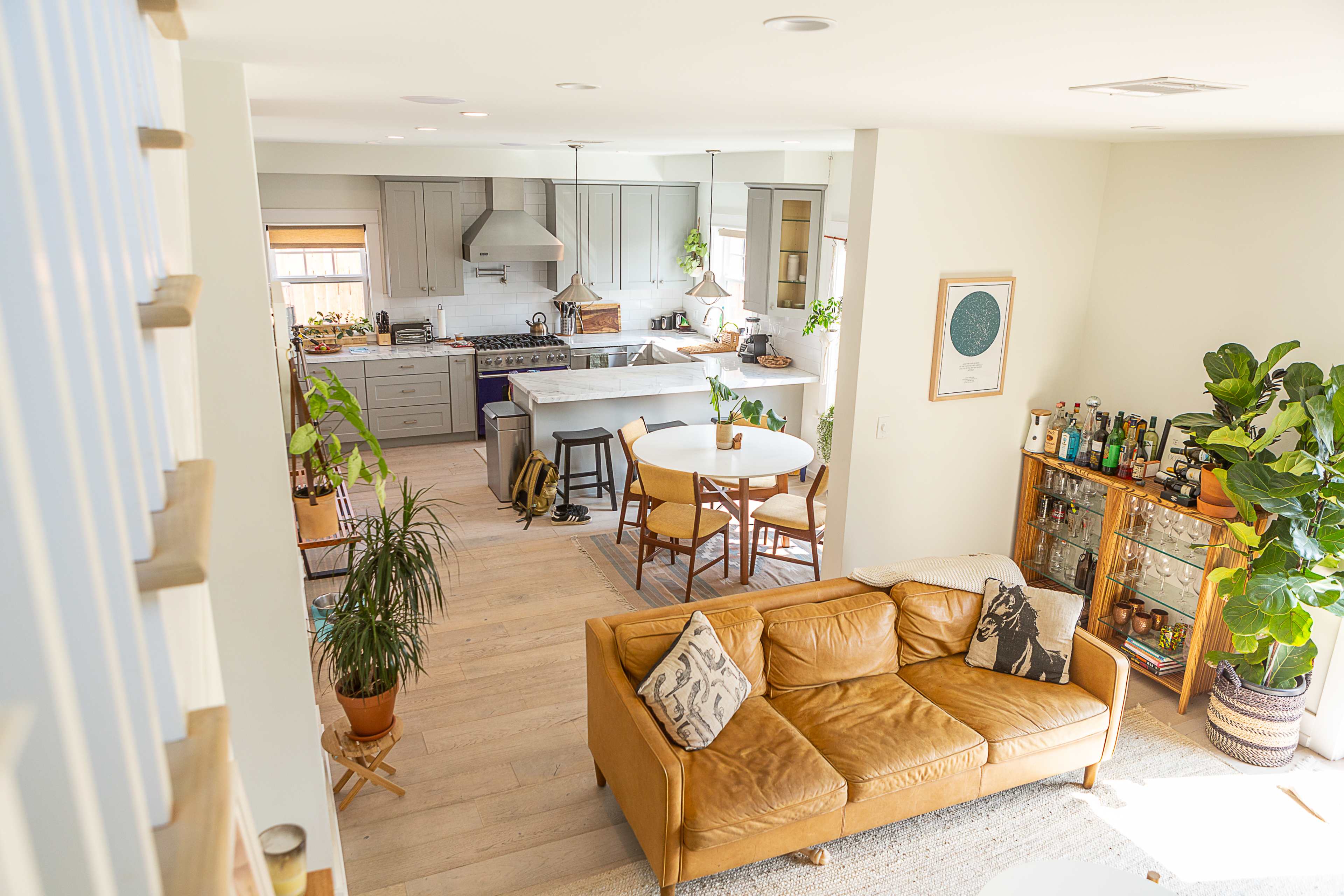 A spacious, modern living area features a brown leather sofa, a round dining table, and an open kitchen with gray cabinets and a large island.