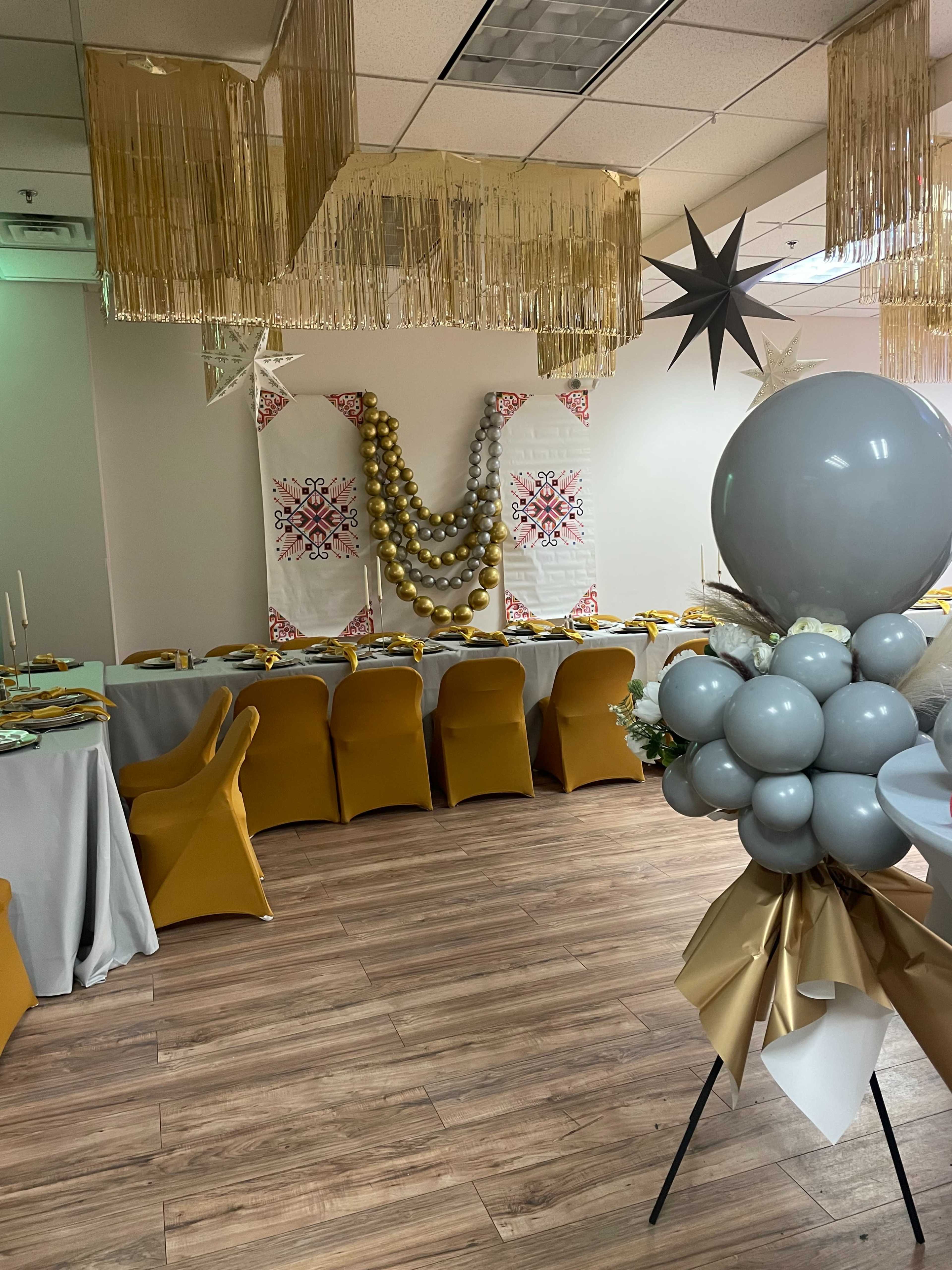 A decorated dining area with a long table set for a celebration, featuring golden balloons, elegant table settings, and decorative wall hangings.