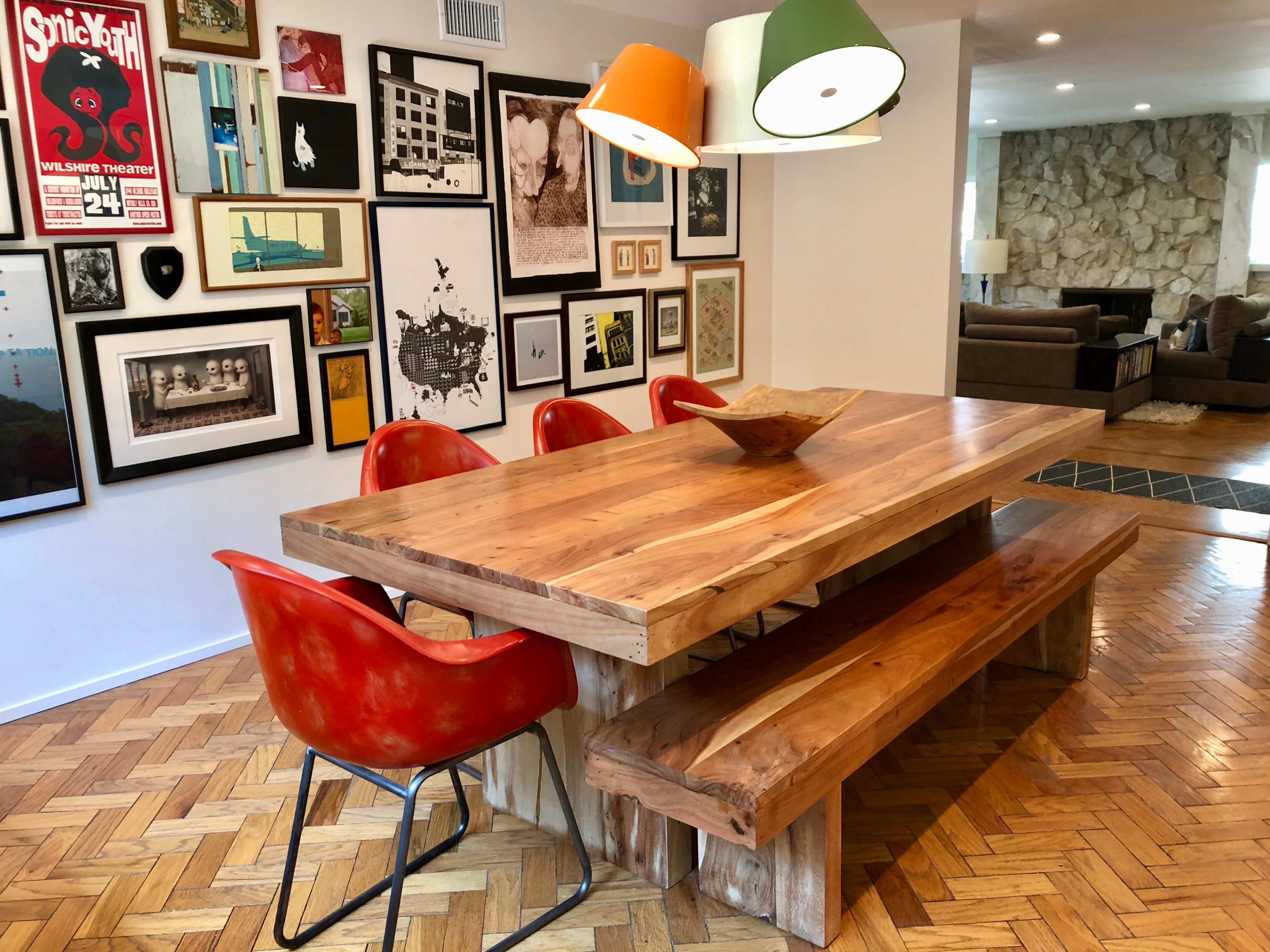 A wooden dining table with red chairs and a centerpiece is situated in a room adorned with a wall of various framed artworks.