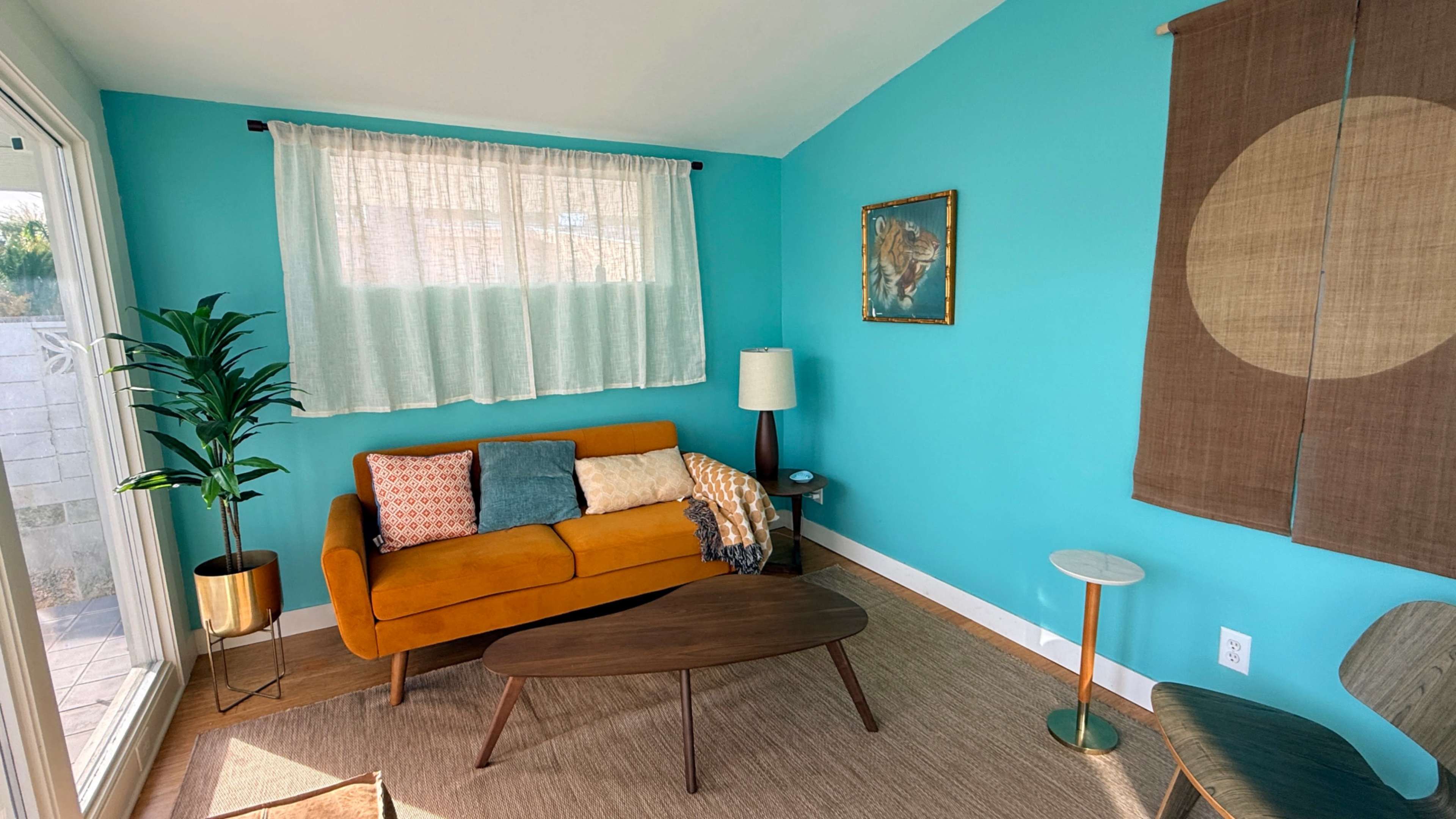 The image shows a living room with a bright turquoise wall, a mustard-colored sofa, a wooden coffee table, and a potted plant.