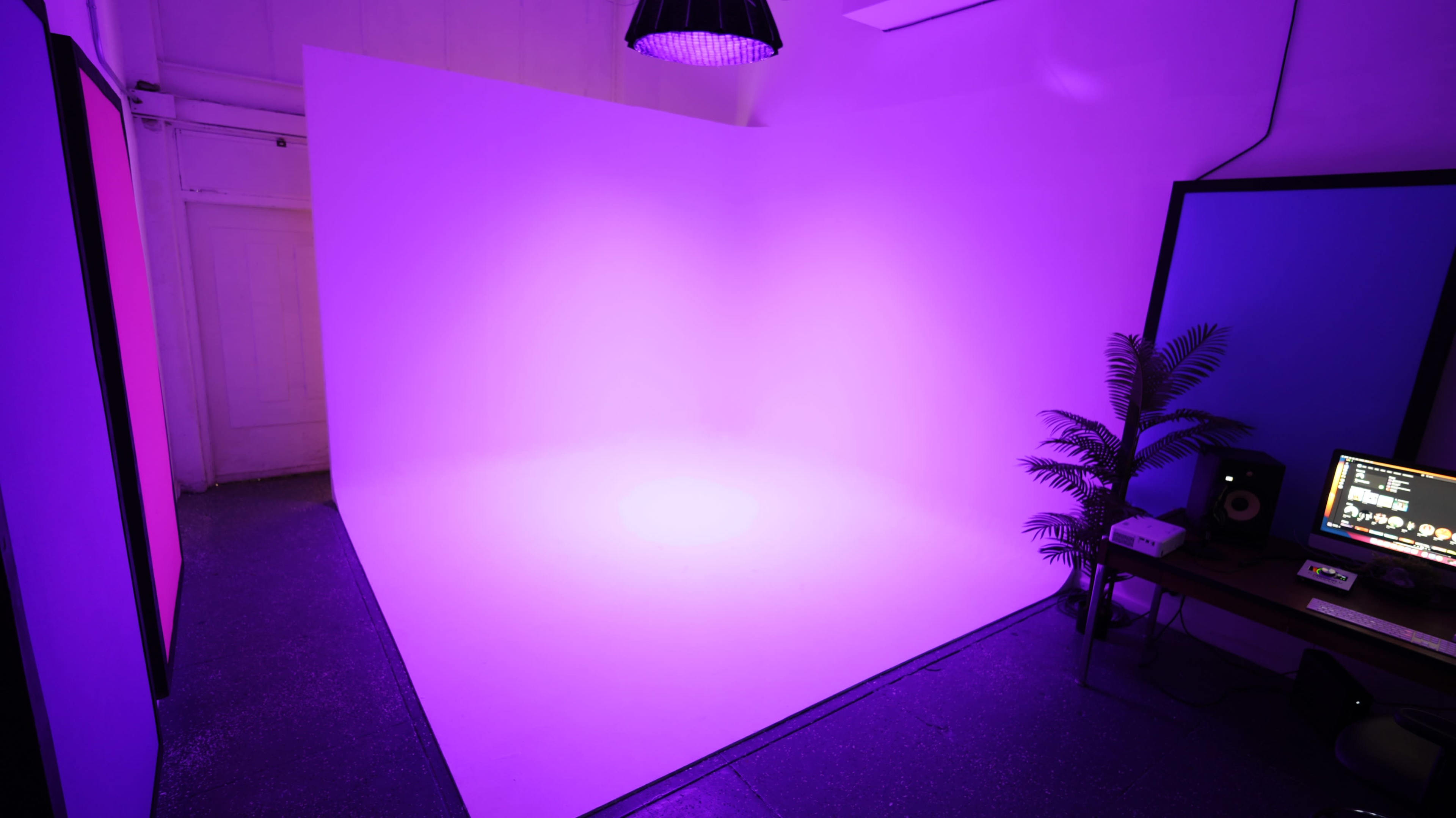 The image shows a well-lit room with a purple backdrop, a plant in the corner, and a table with equipment.