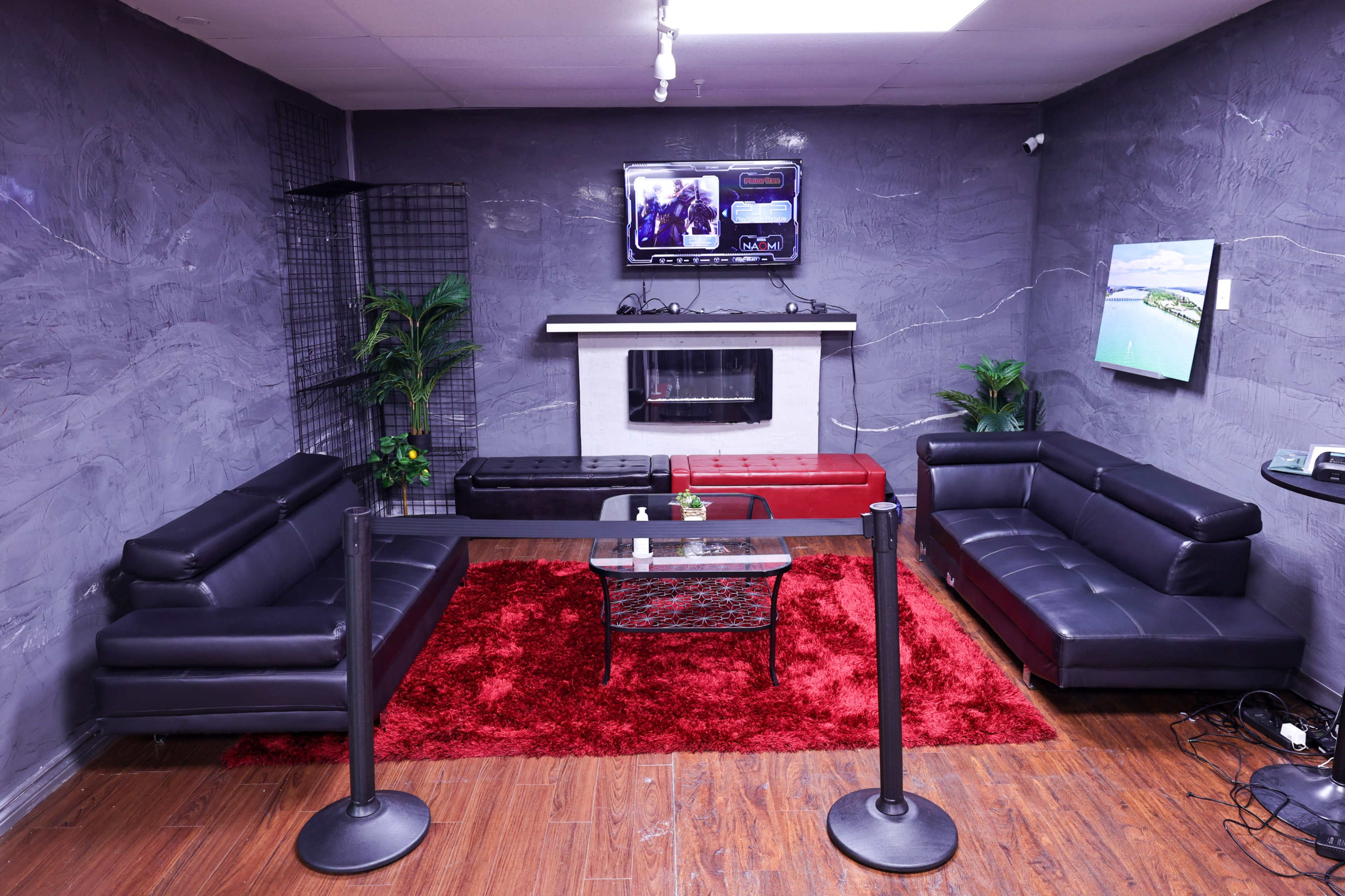 A modern lounge area with two black sofas, a red rug, a coffee table, and a wall-mounted television above a white fireplace.
