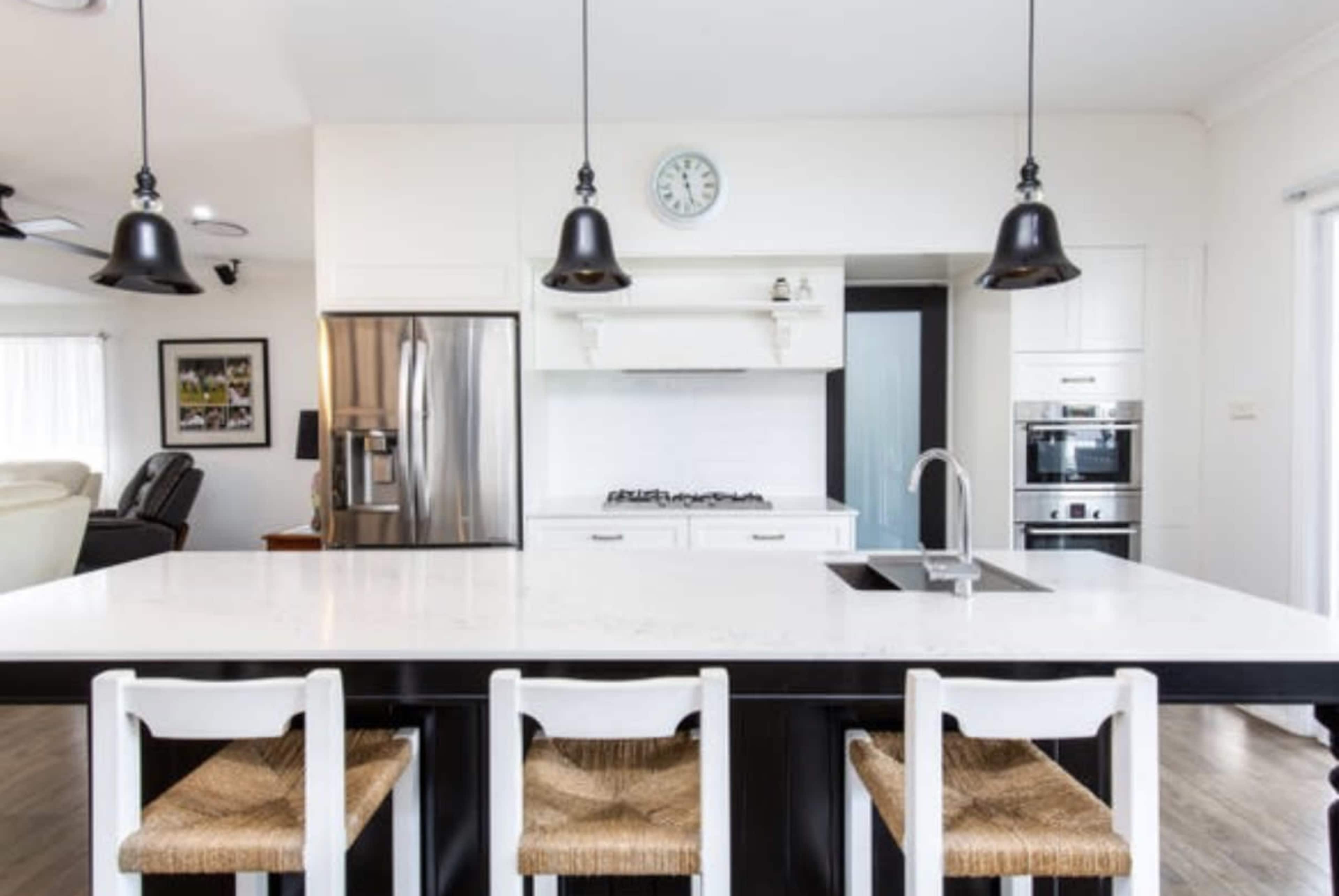 A modern kitchen features a large white island with black seating, stainless steel appliances, and pendant lighting.