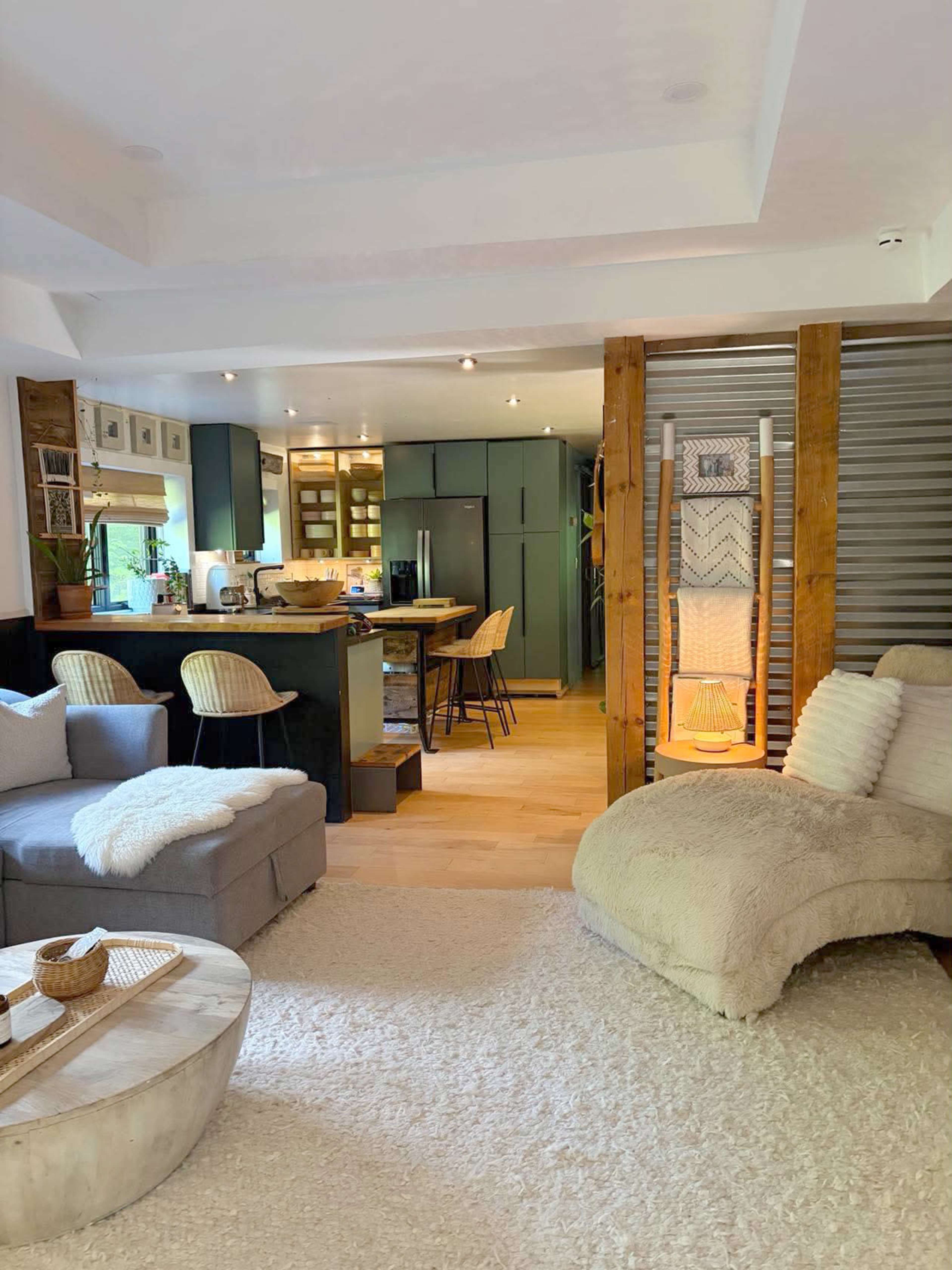 The image depicts a modern, open-concept living space featuring a cozy seating area with a light-colored rug, a wooden coffee table, and a kitchen in the background.