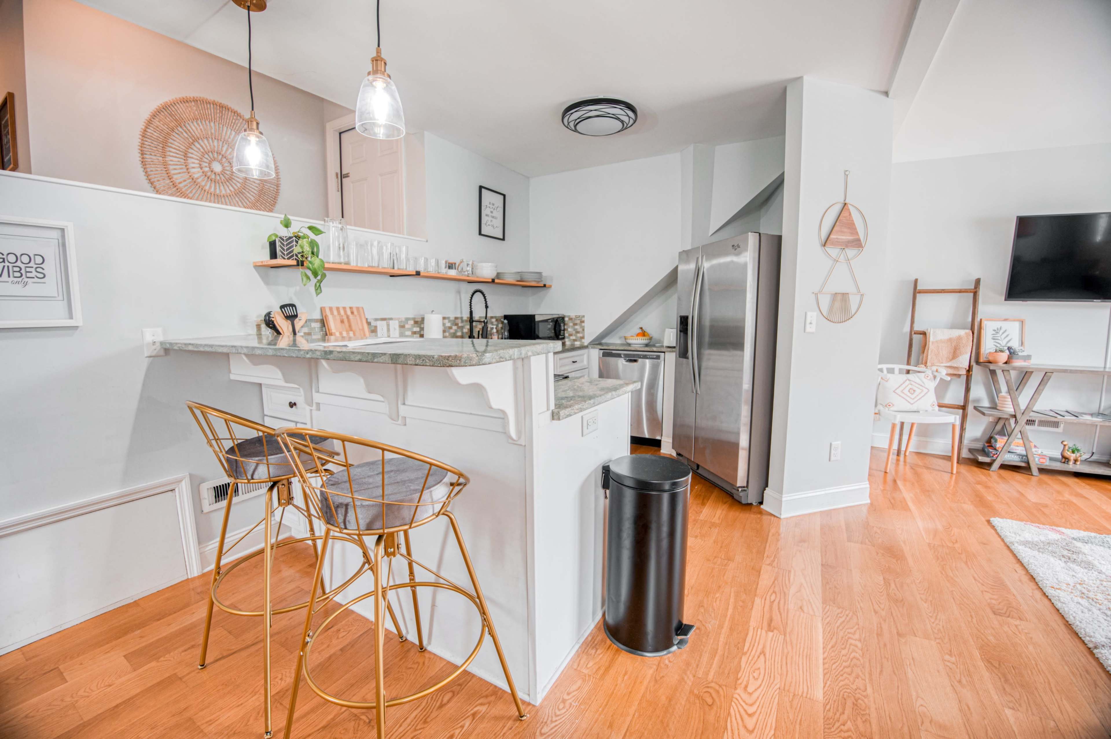 A modern kitchen featuring a bar area with two stools, stainless steel appliances, and light-colored cabinetry.