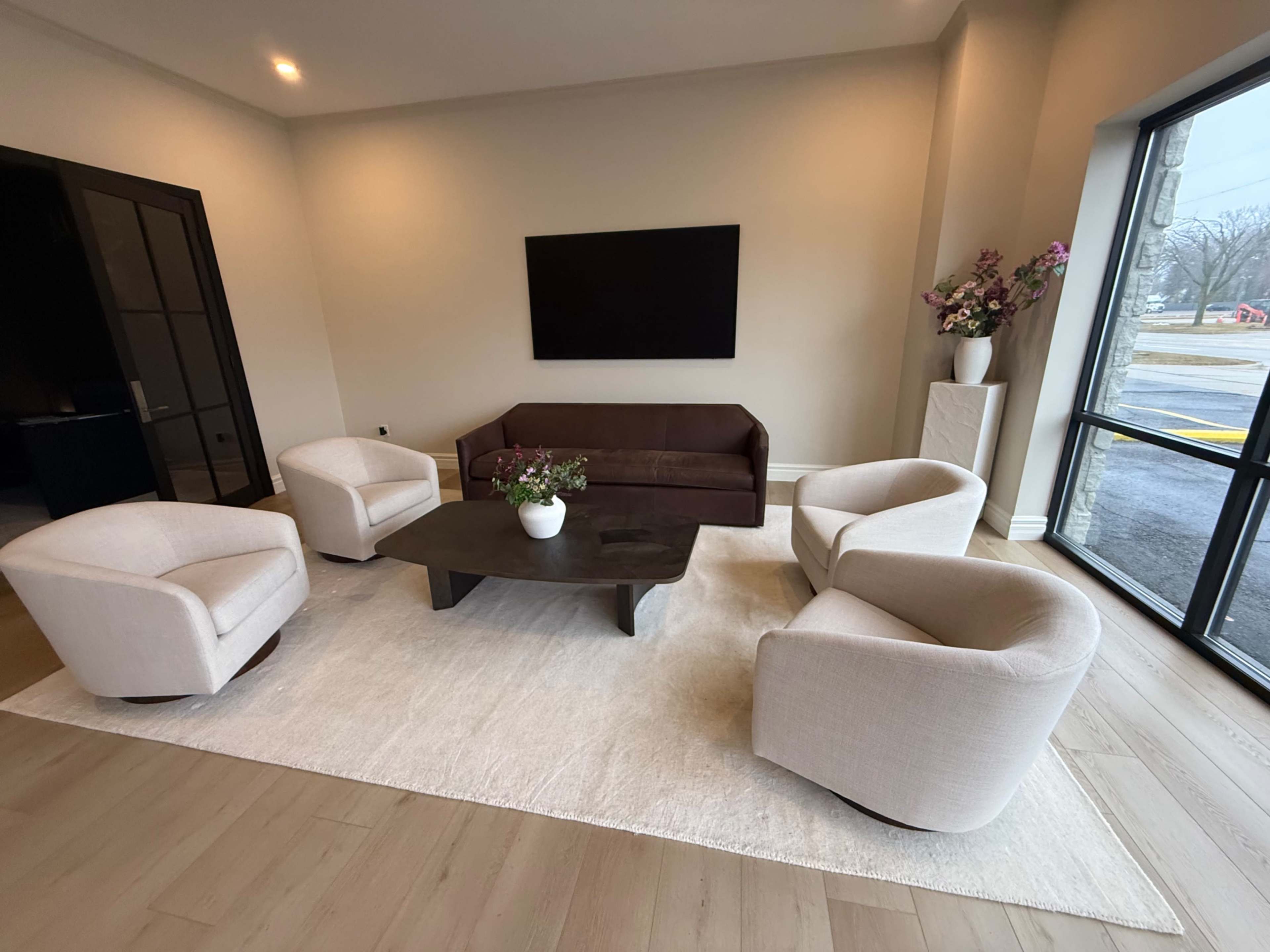 The image shows a modern seating area with a dark sofa and four light armchairs arranged around a dark coffee table on a light rug.