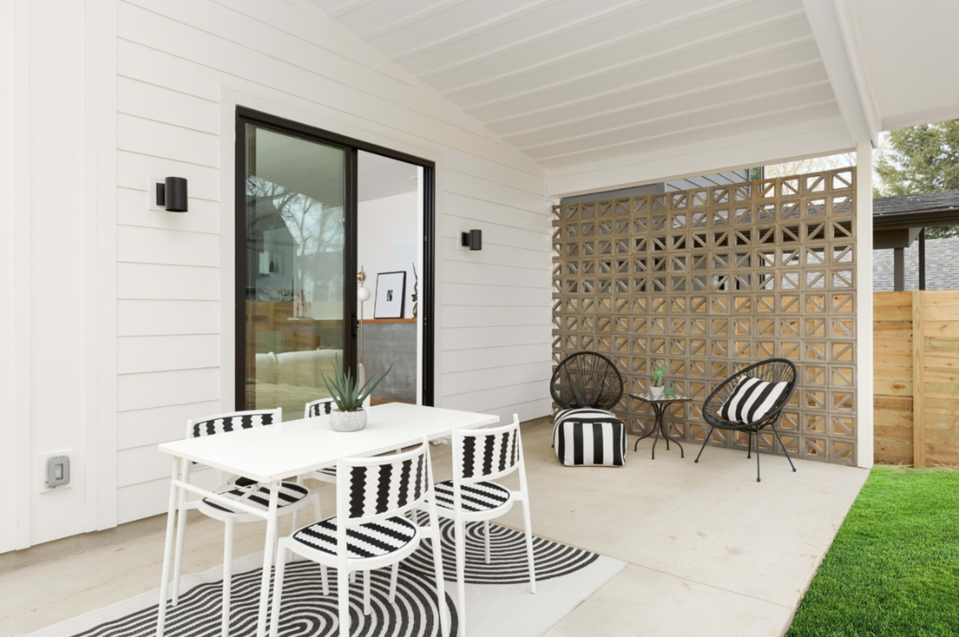The image shows a modern outdoor patio with a white table and striped chairs, situated next to a decorative brick wall and a green lawn.