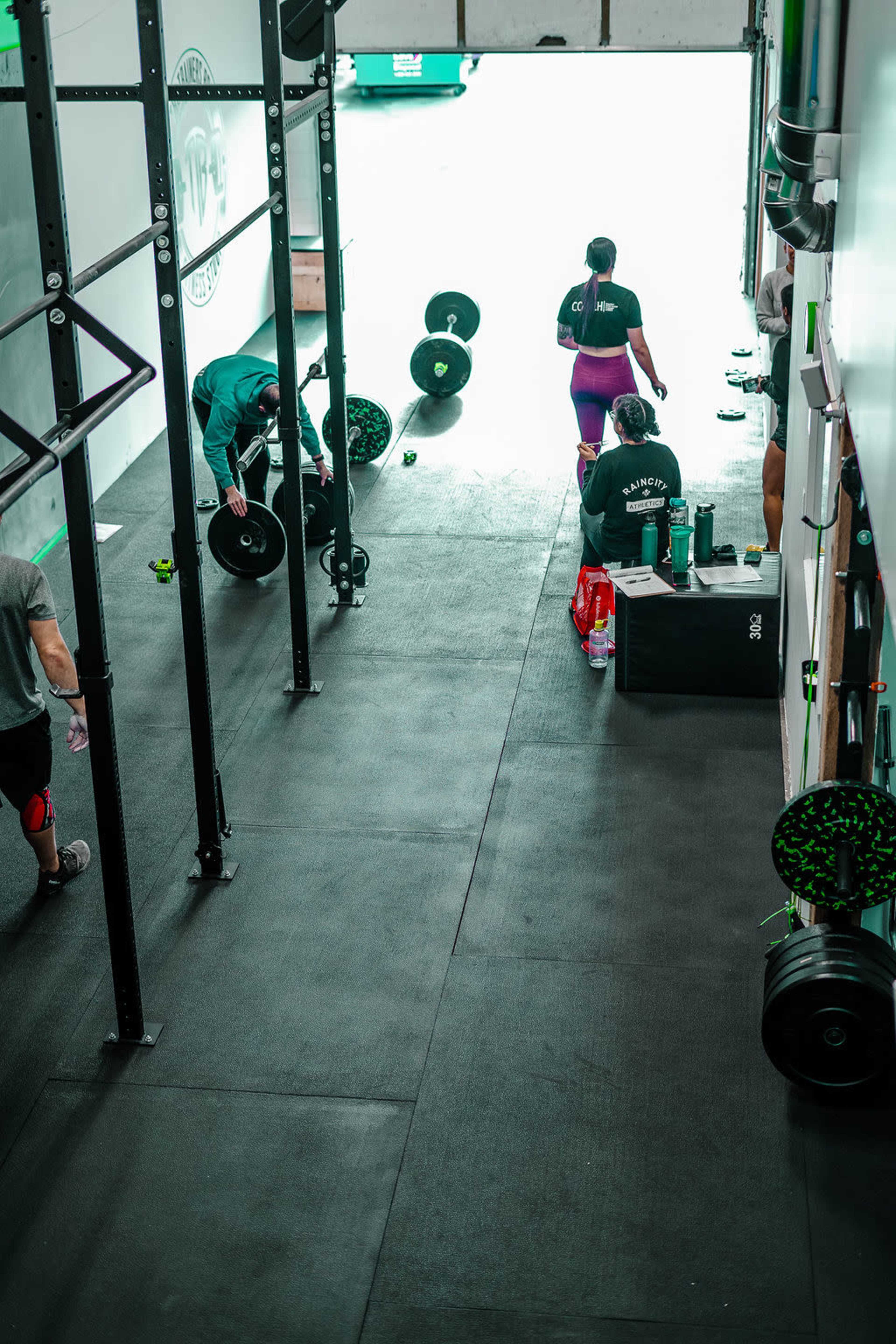 A gym interior features several individuals engaging with weights and exercise equipment.