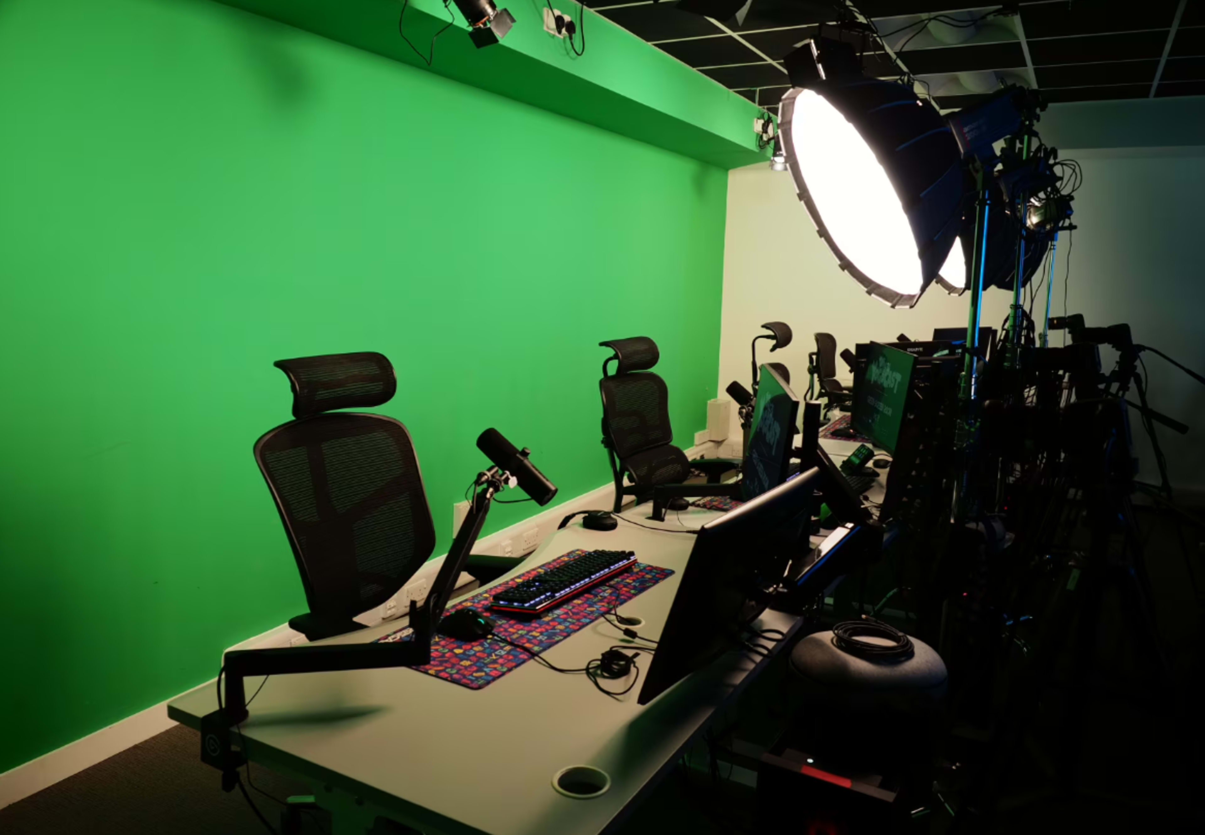 The image shows an empty studio setup with green walls, multiple computer workstations, and studio lighting equipment arranged along one side.