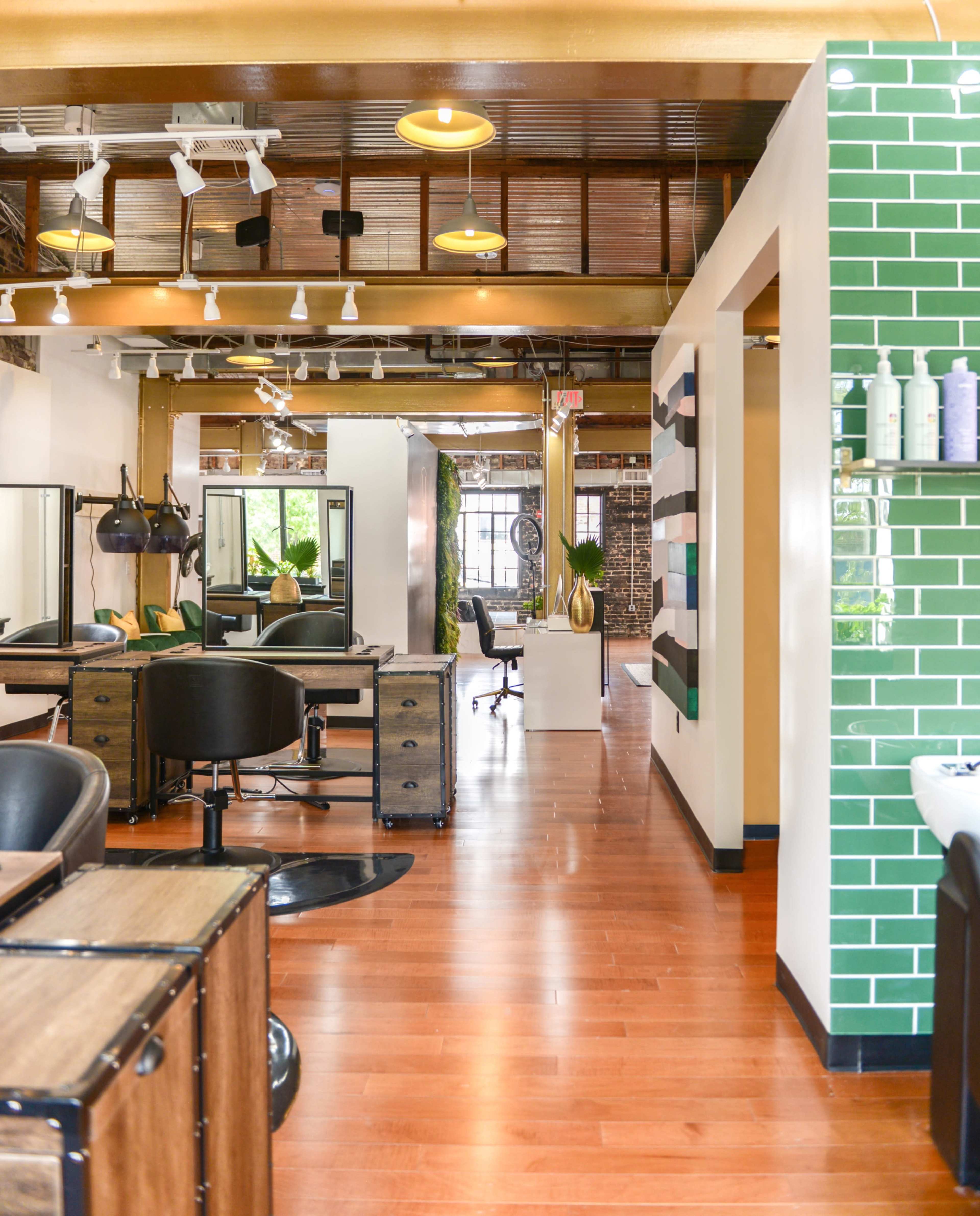 The image shows a modern hair salon with several styling stations and green tiled walls.