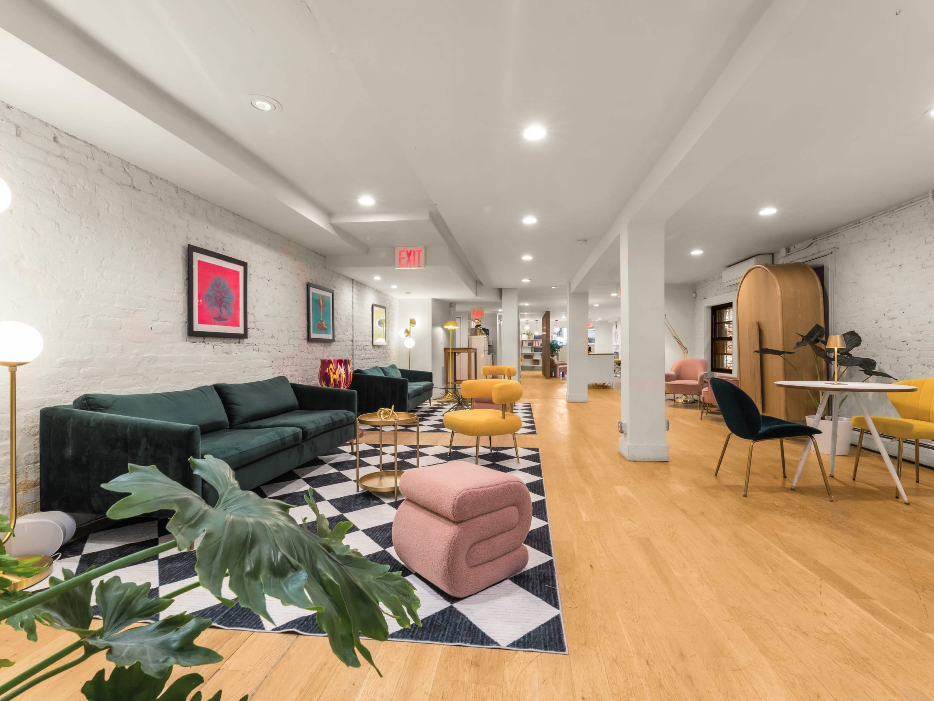 The image features a modern, open lounge area with a mix of seating options, including a green sofa and colorful chairs, set against a backdrop of exposed brick walls and wooden flooring.