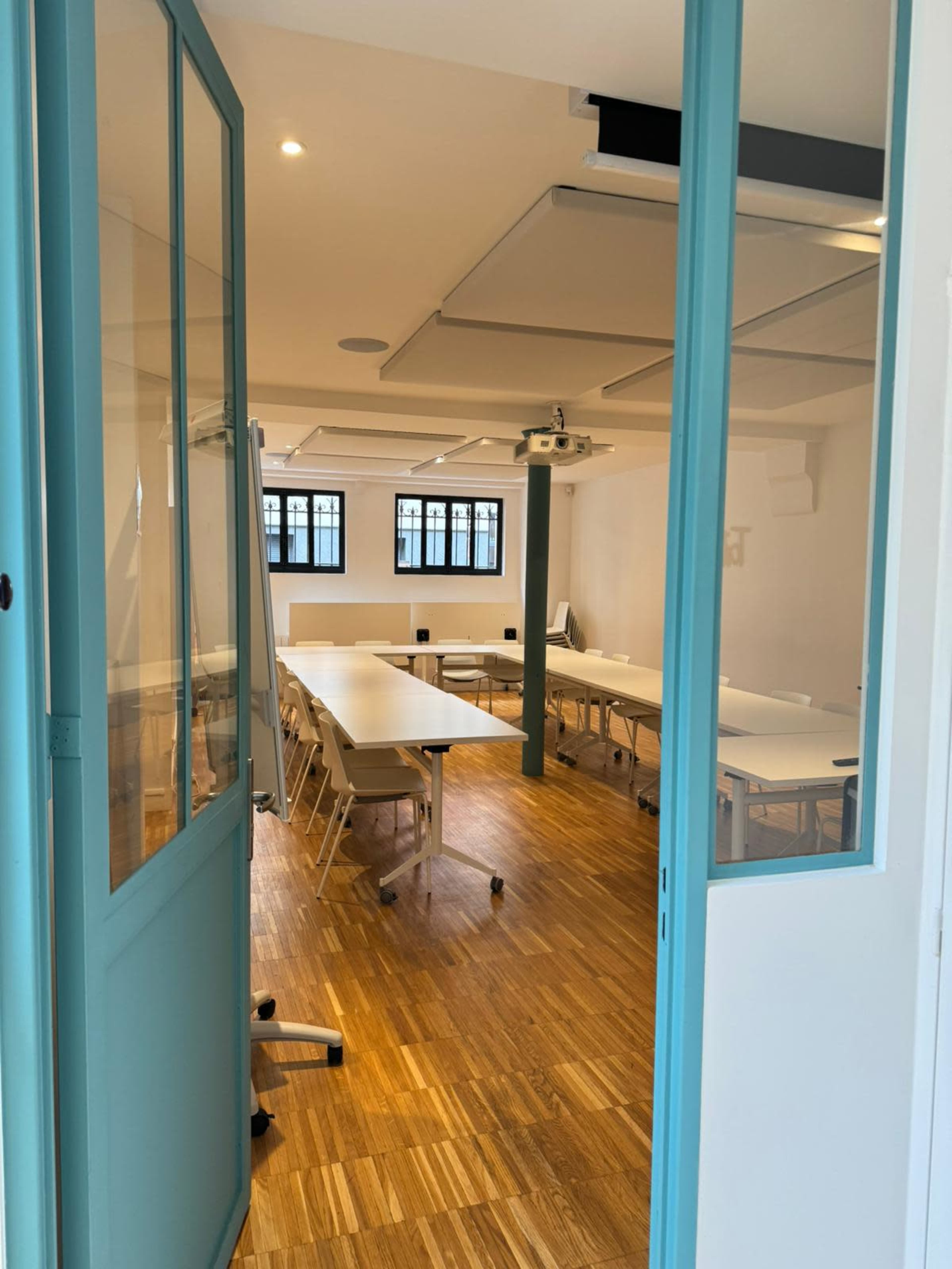A spacious conference room with tables and chairs is visible through a glass door, featuring wooden flooring and a projector mounted on the ceiling.