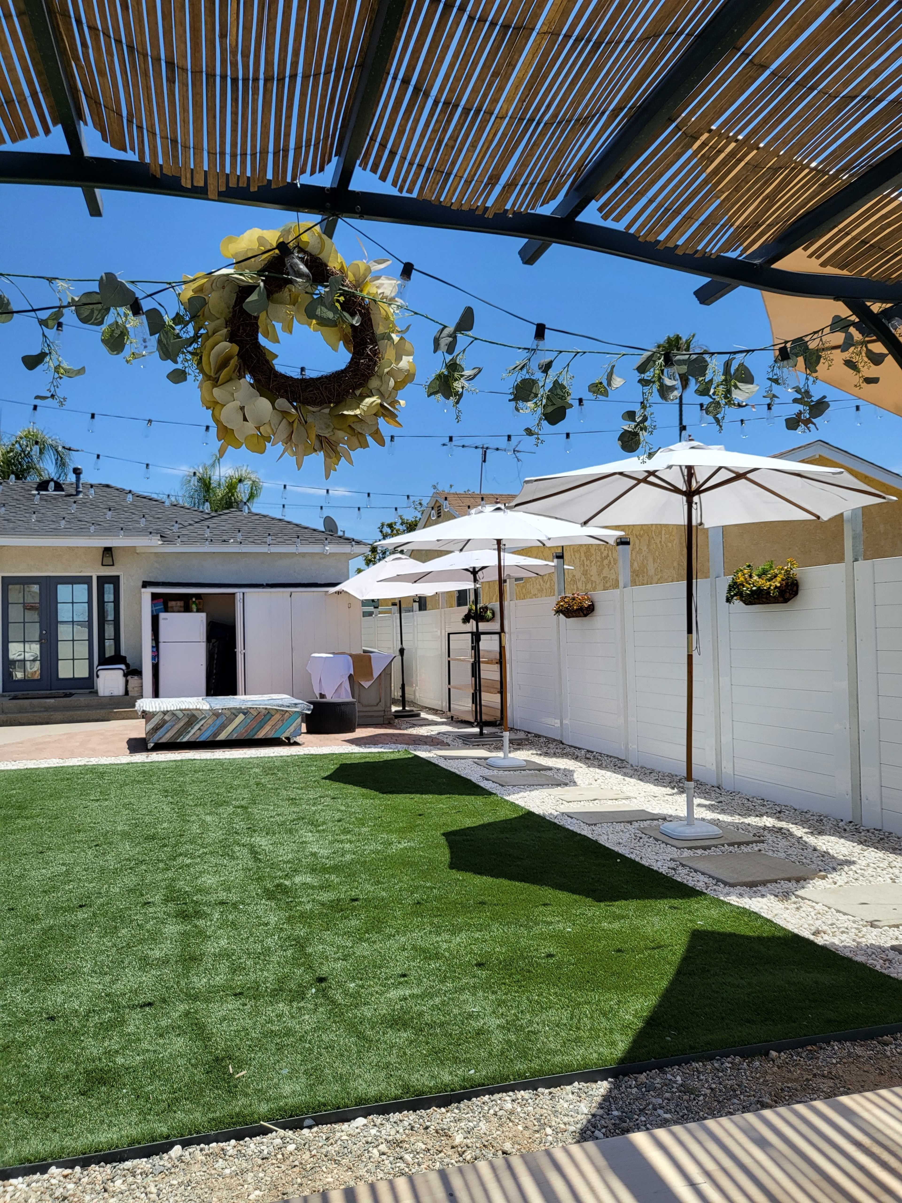 A backyard space with artificial grass, patio umbrellas, a seating area, and decorative string lights overhead.