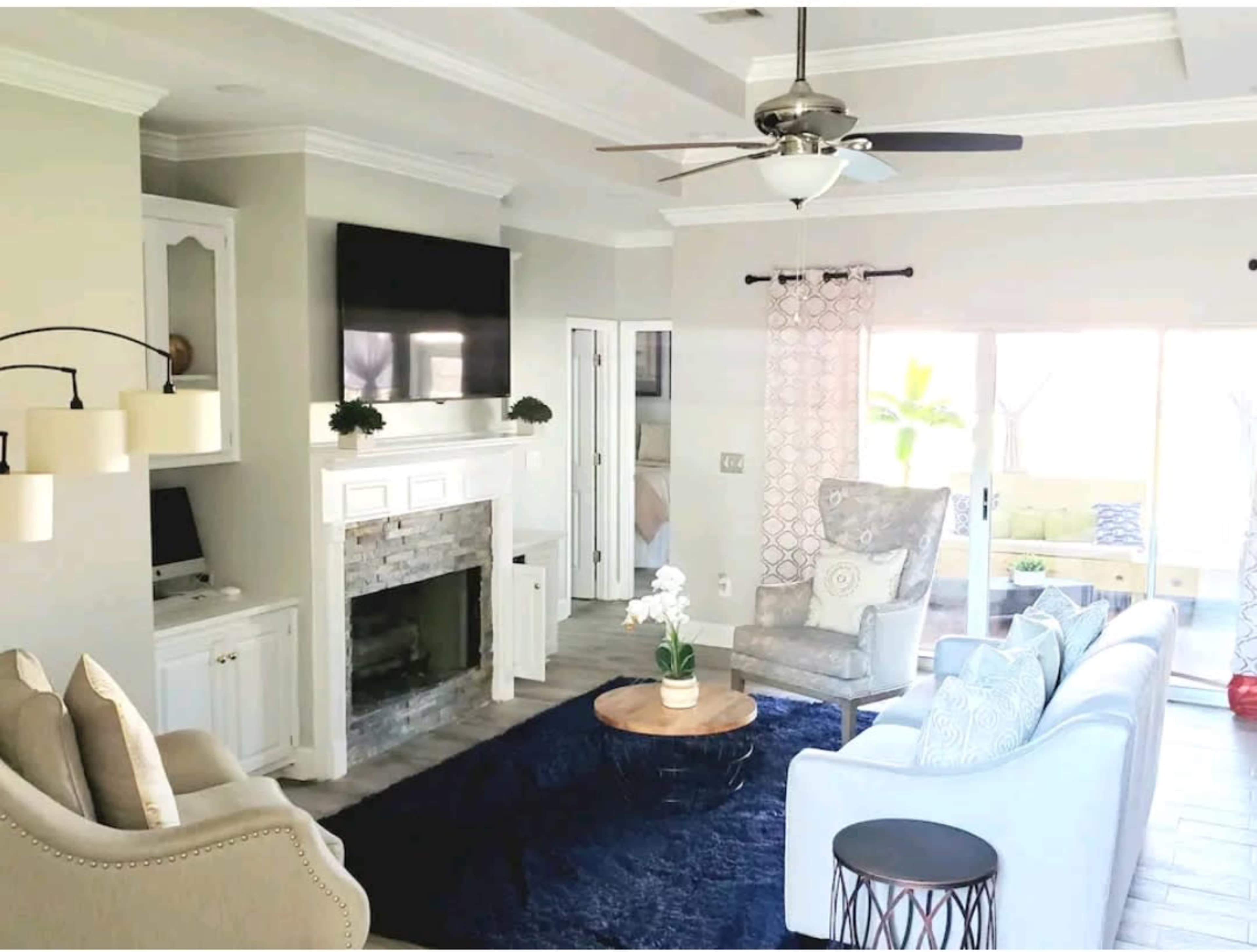 A well-decorated living room with a stone fireplace, a ceiling fan, and a mix of modern and traditional furniture.