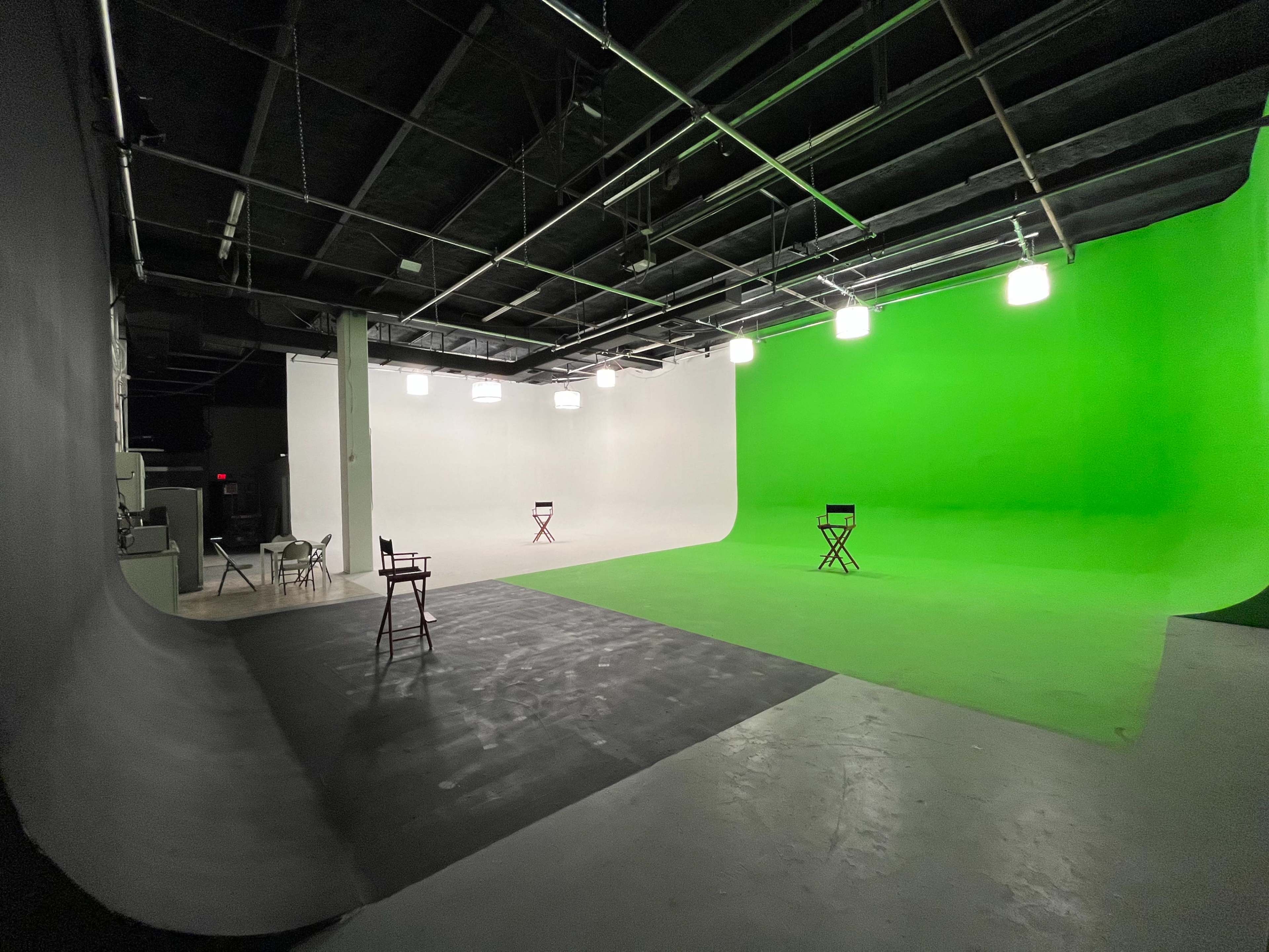 The image shows a studio setup with two colored backdrops, one green and one white, and several director's chairs positioned in front of them.