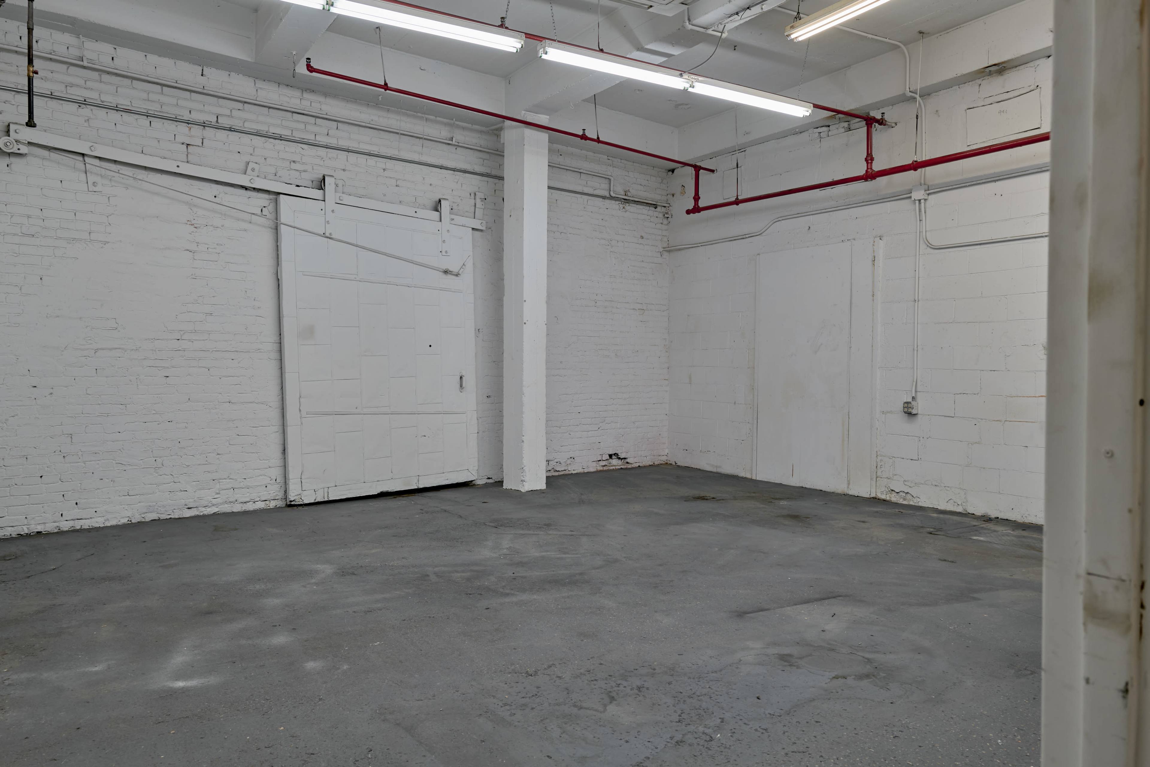 The image shows an empty industrial space with white brick walls and gray concrete flooring.