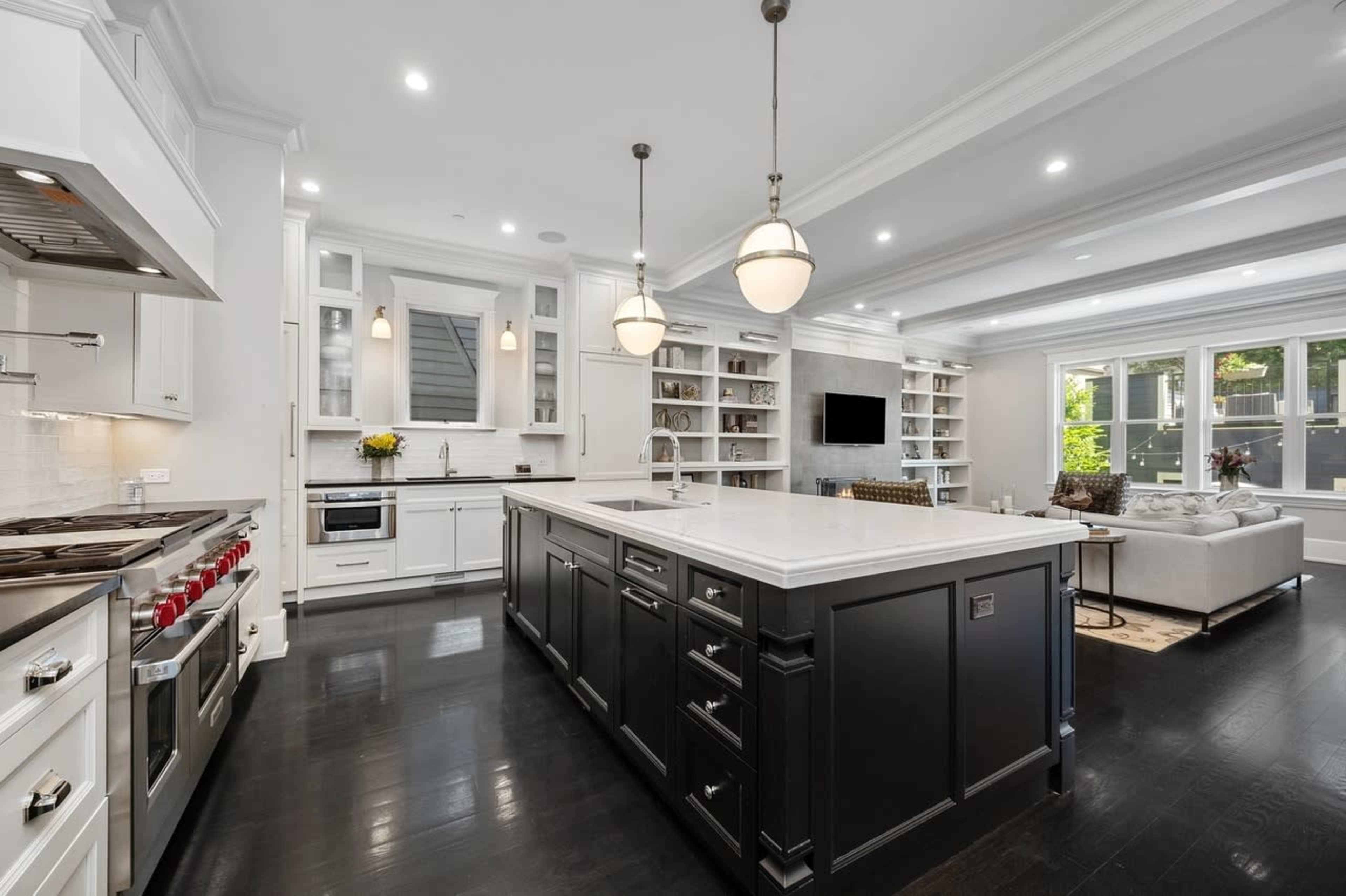 A modern kitchen features an island with a white countertop, dark cabinetry, and stainless steel appliances, illuminated by pendant lights.
