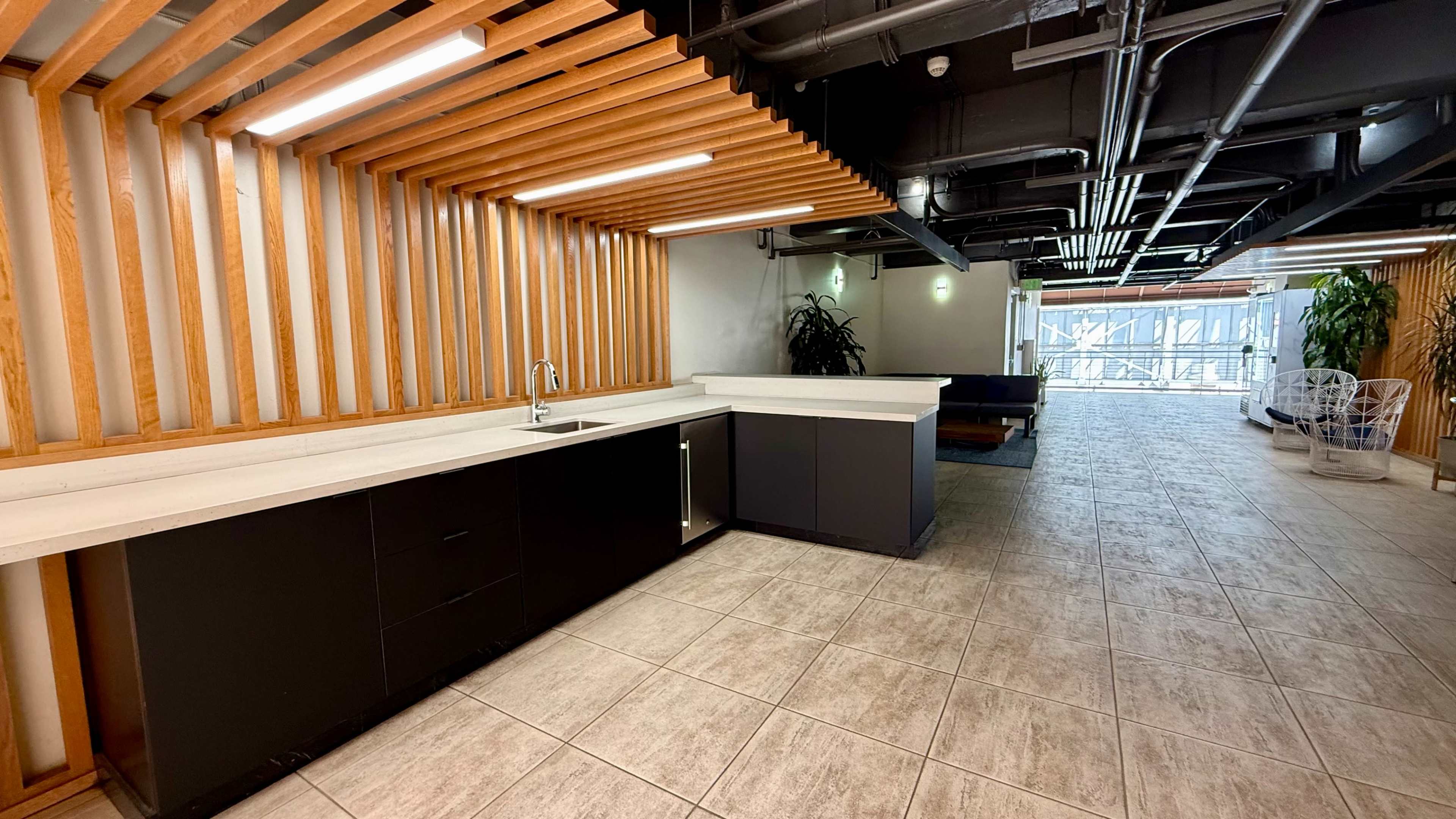 The image shows a modern kitchen area with a long countertop, cabinets, and wooden slat walls, leading to a spacious corridor.