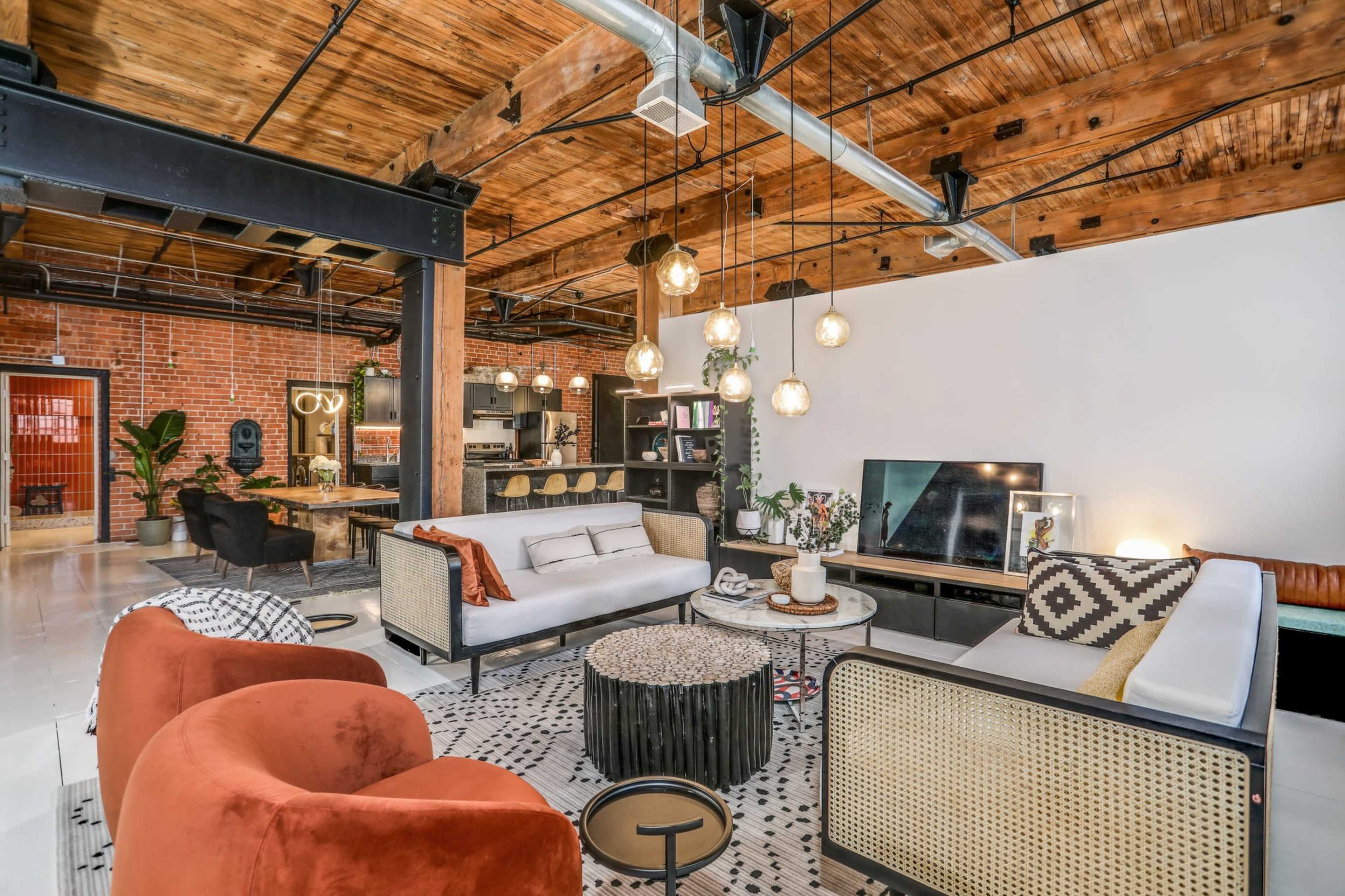A spacious living area with exposed wooden beams, a mix of modern and vintage furniture, and decorative plants.