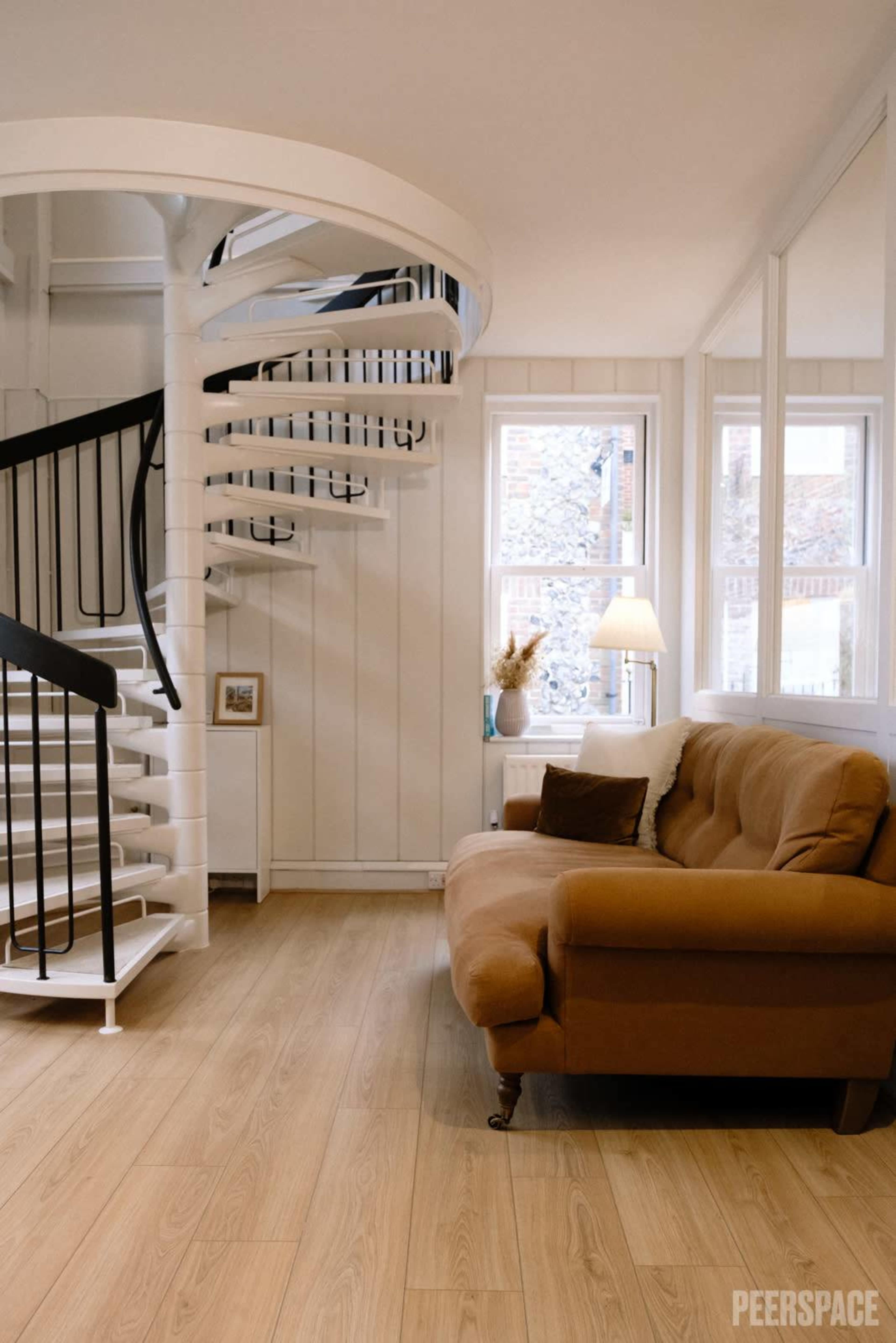 A cozy living area featuring a brown couch, a spiral staircase, and a window with natural light.