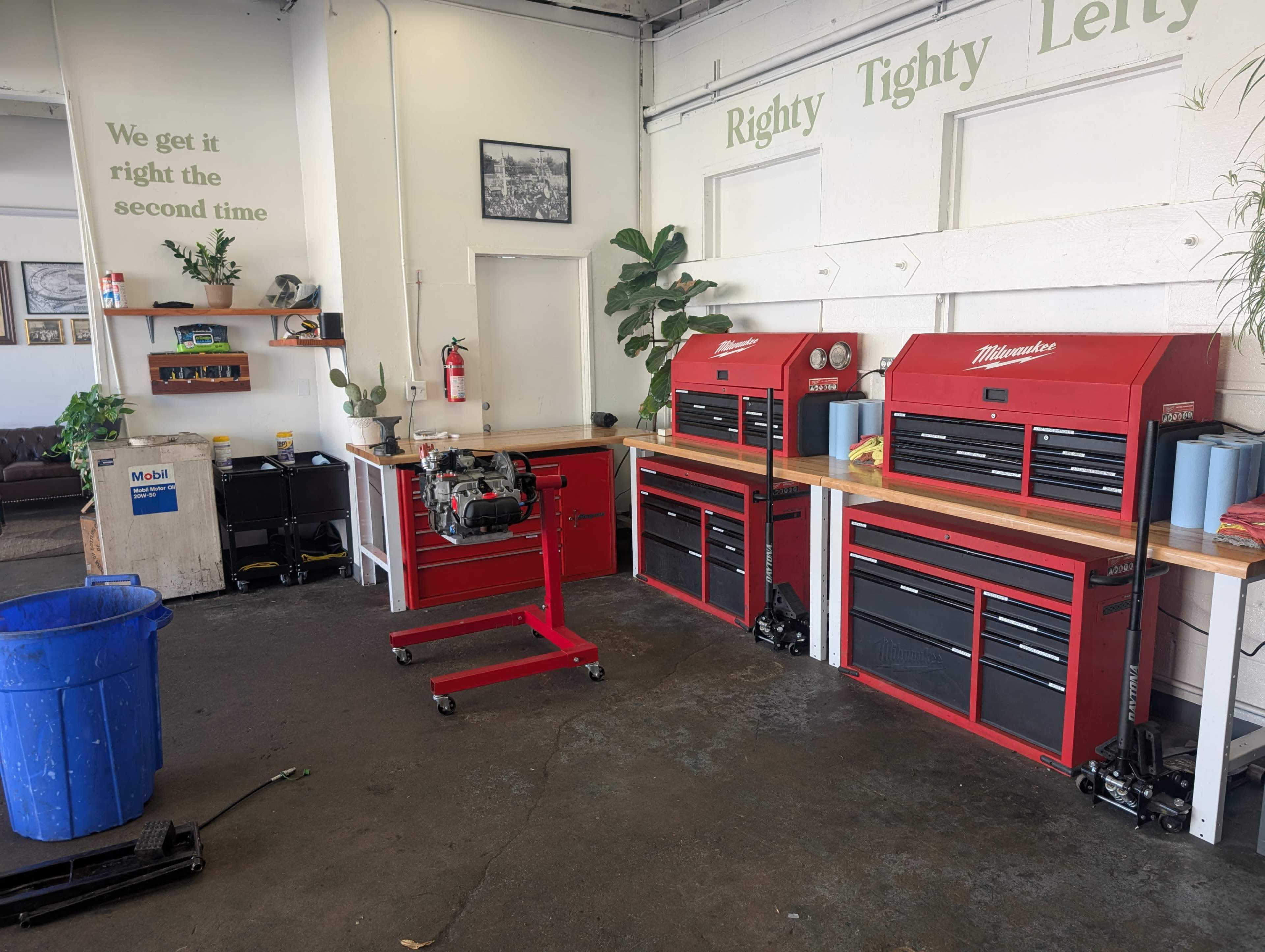 The image shows a garage workspace featuring two red tool chests, a workbench with a small engine, and a blue trash bin in a well-lit area.