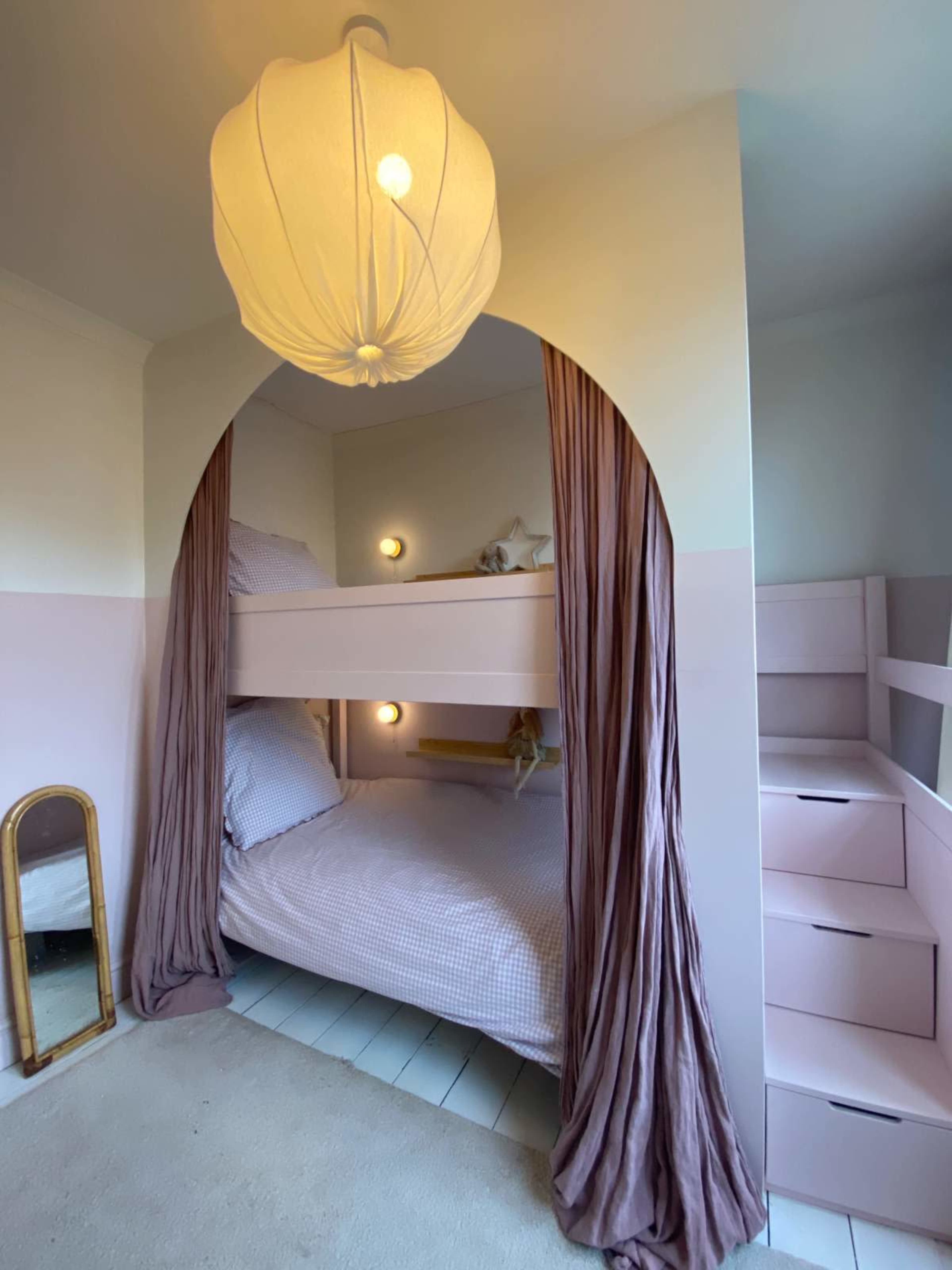 The image shows a children's bedroom with a bunk bed, soft drapes, and a large pendant light, along with a mirror and shelving unit.