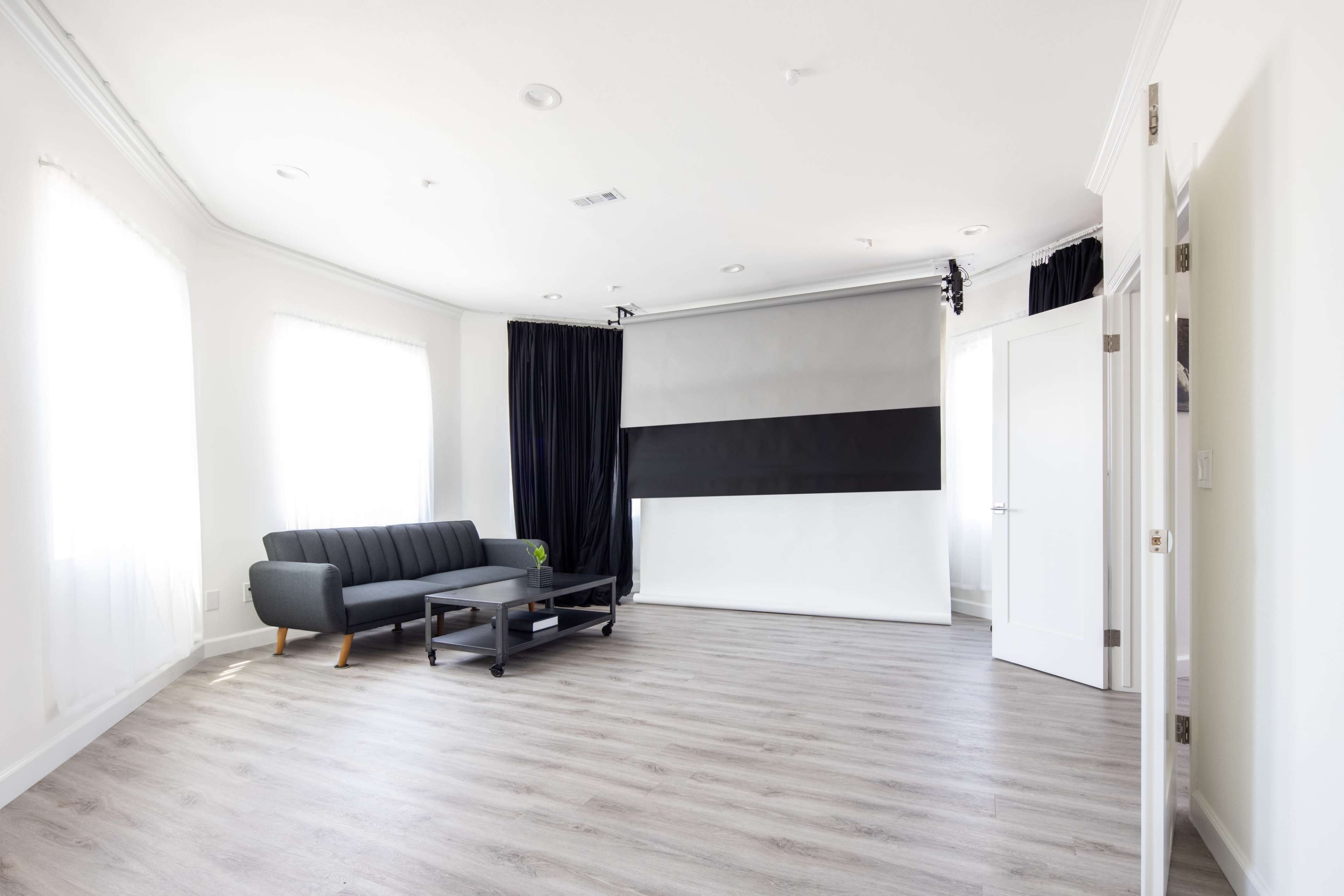 A spacious room with a gray sofa, a black coffee table, and large windows covered by sheer white curtains.