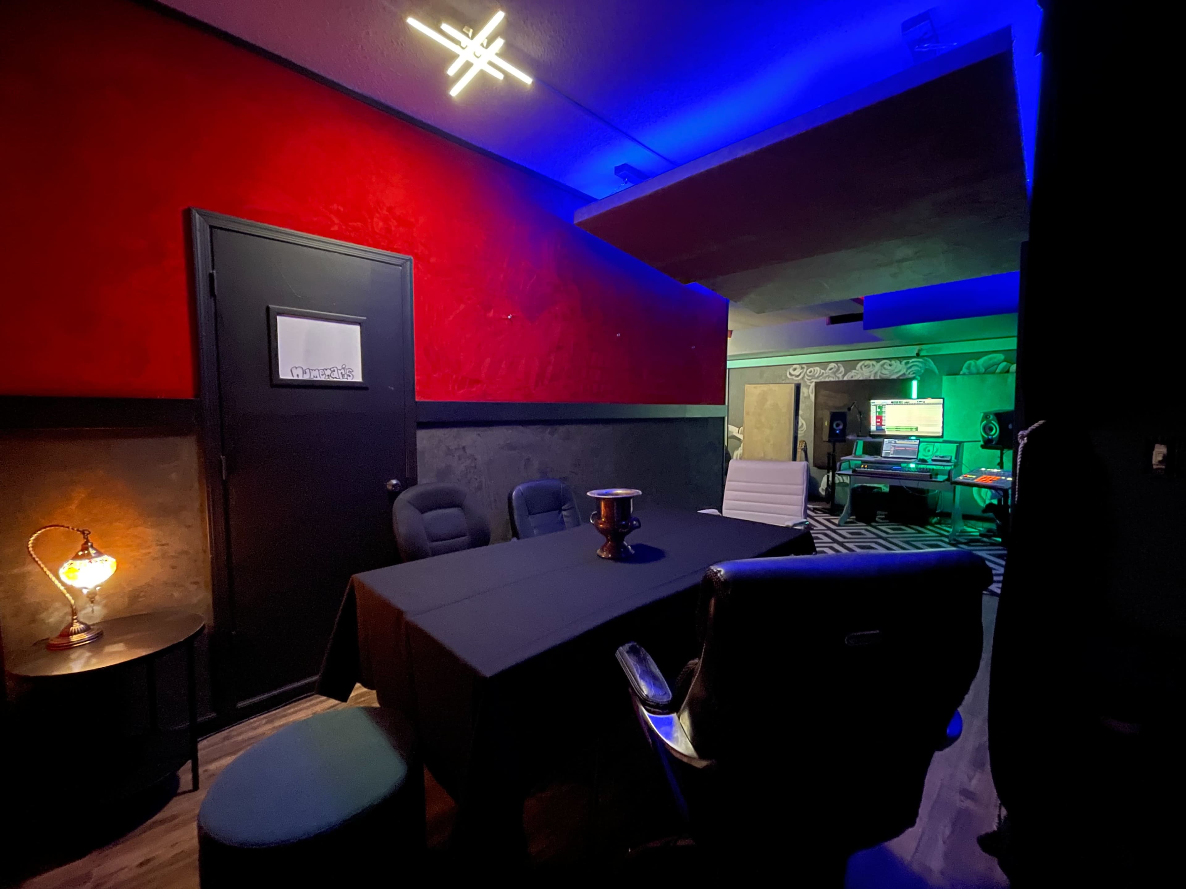 A dimly lit room features a black table surrounded by chairs, with a red accent wall and blue lighting in the background.