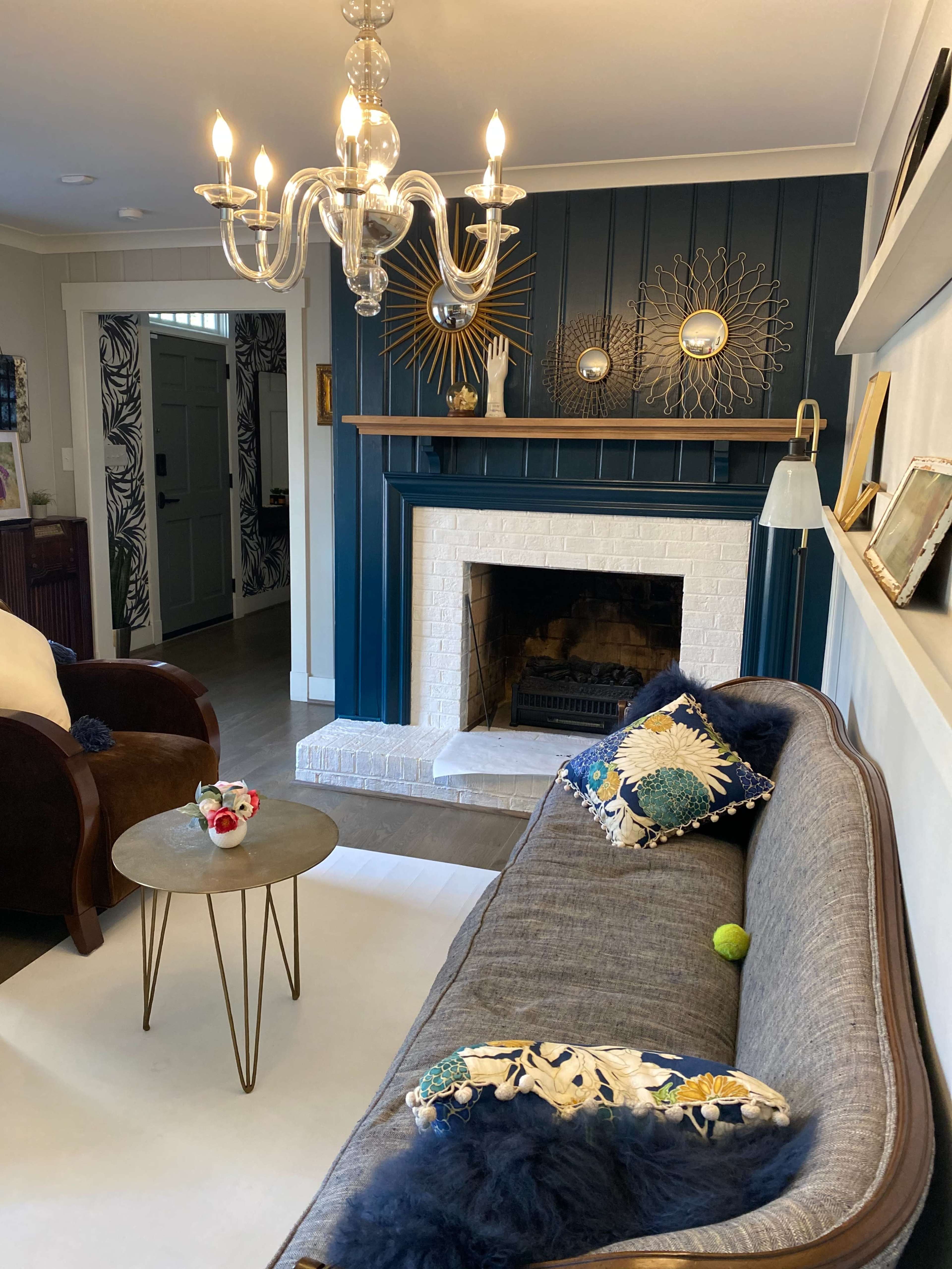 A cozy living room with a blue accent wall, a white-brick fireplace, a modern chandelier, and a couch adorned with decorative pillows.