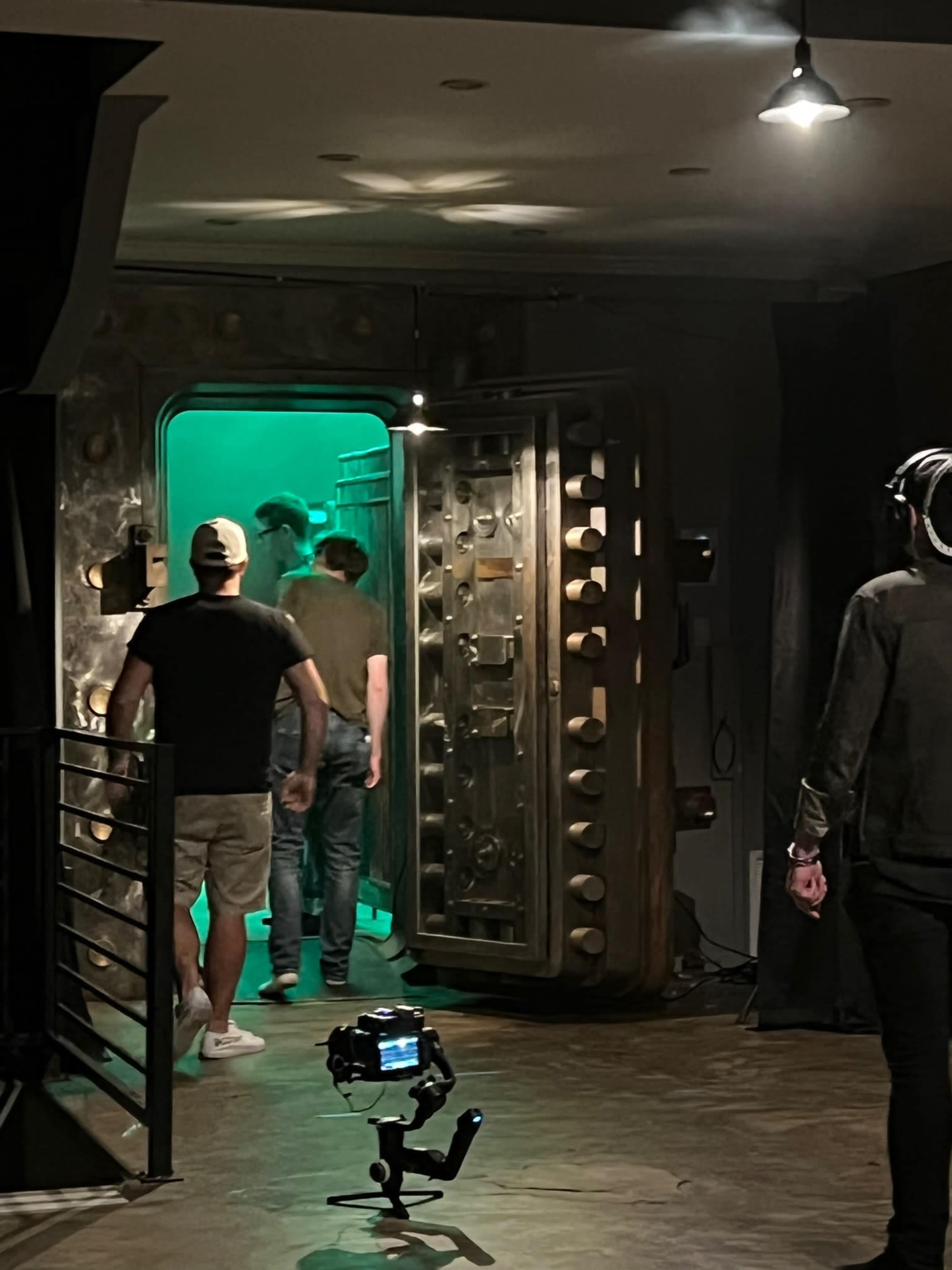 A group of people walks toward a large, illuminated vault door in a dimly lit space.