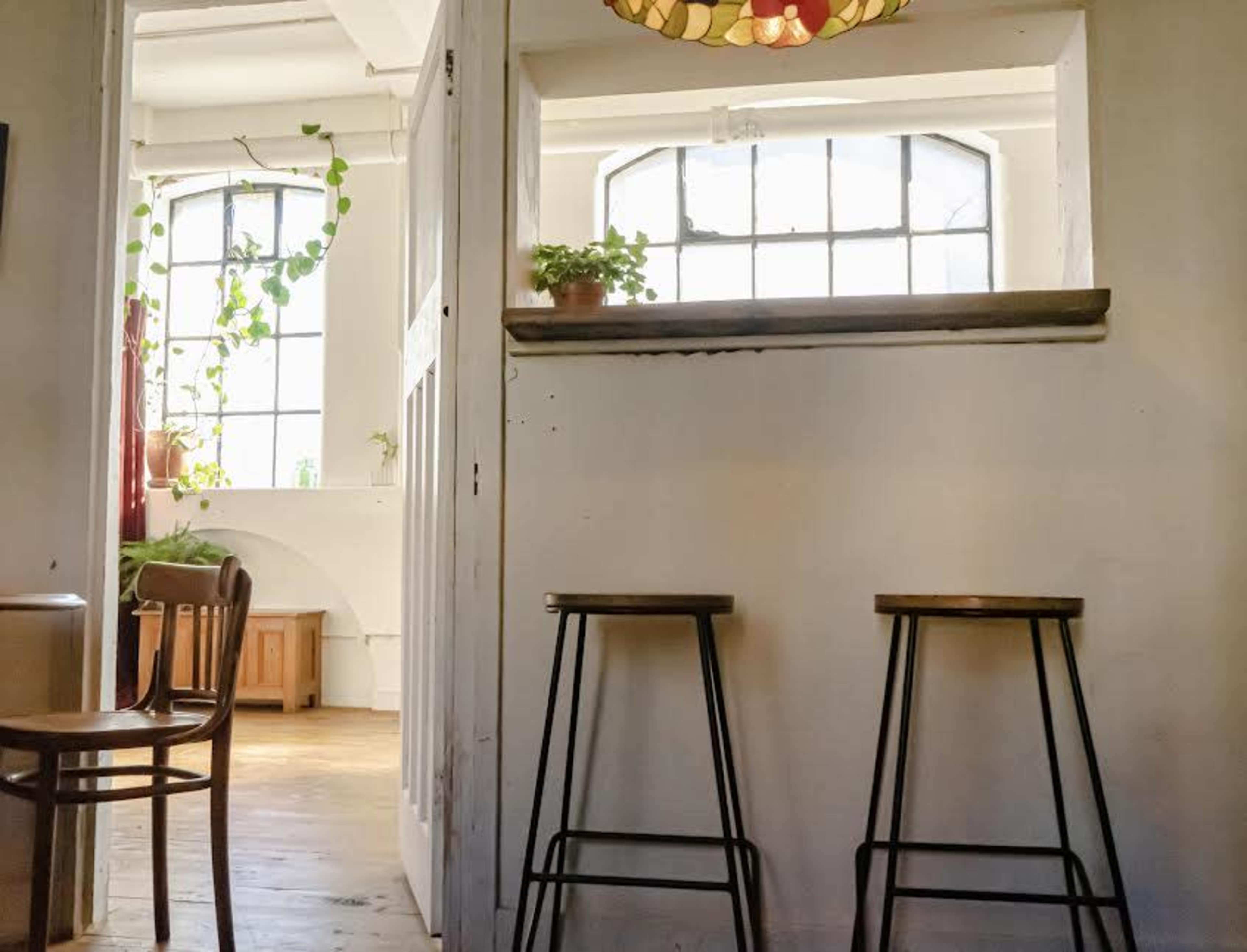 A room with a doorway leading to another area, featuring two metal stools and a window with a plant on the sill.