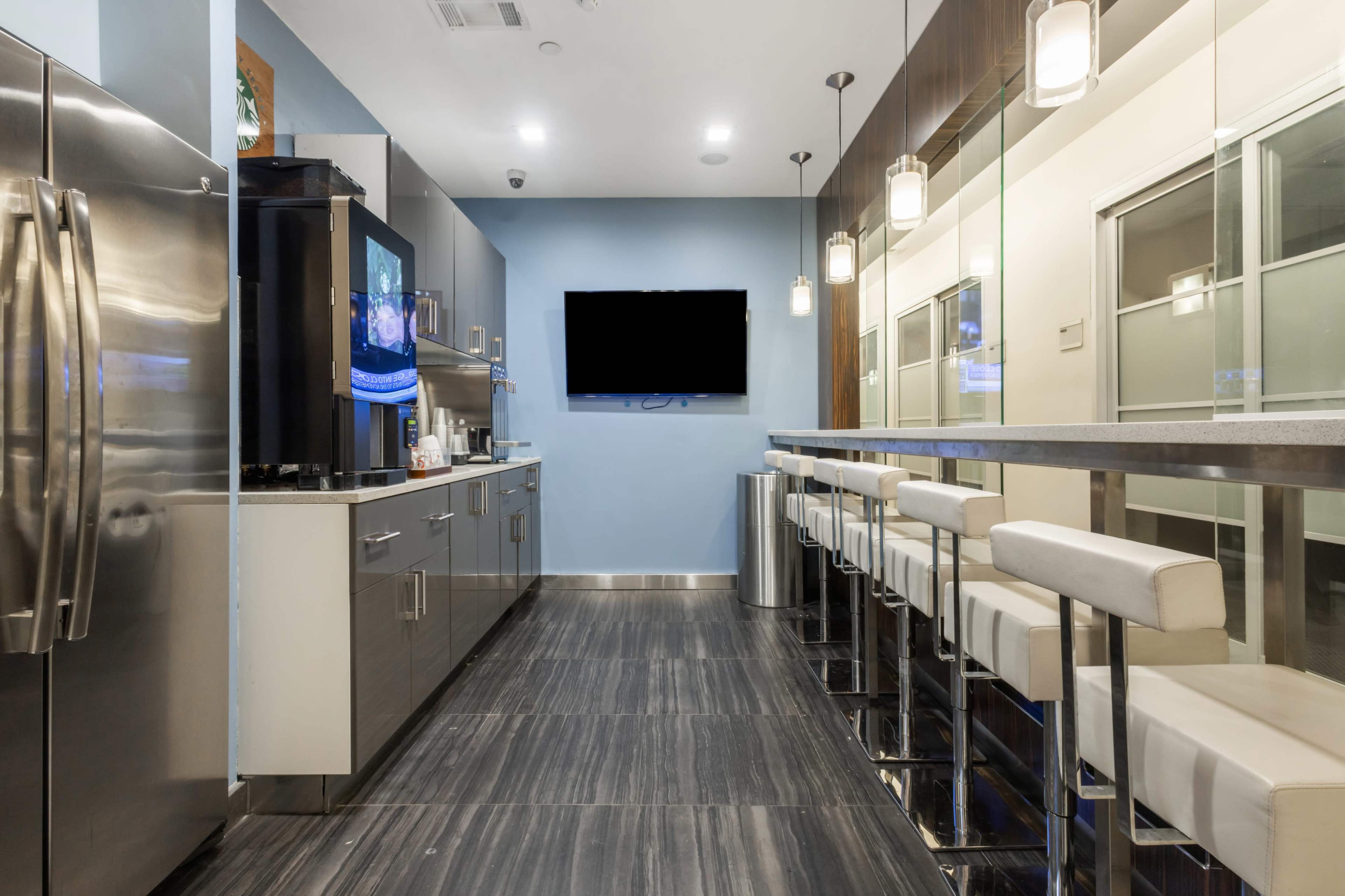 A modern kitchen with stainless steel appliances, a bar with white stools, and a wall-mounted television.